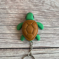 Top of a 3D printed turtle-shaped keychain with brown shell and green body on a wooden surface