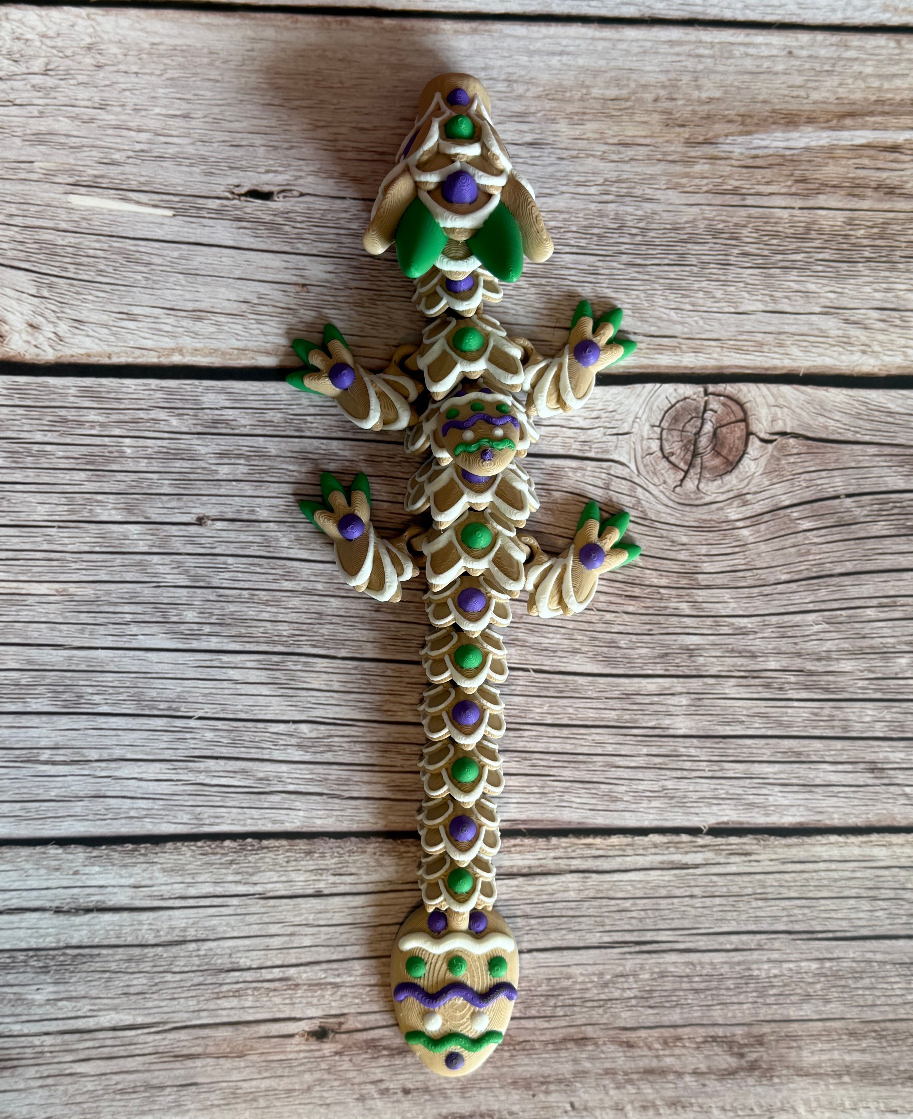 Top of a 3D printed articulated dragon figure resembling a cookie with beige, green, purple, and white colors. Placed on a wooden surface
