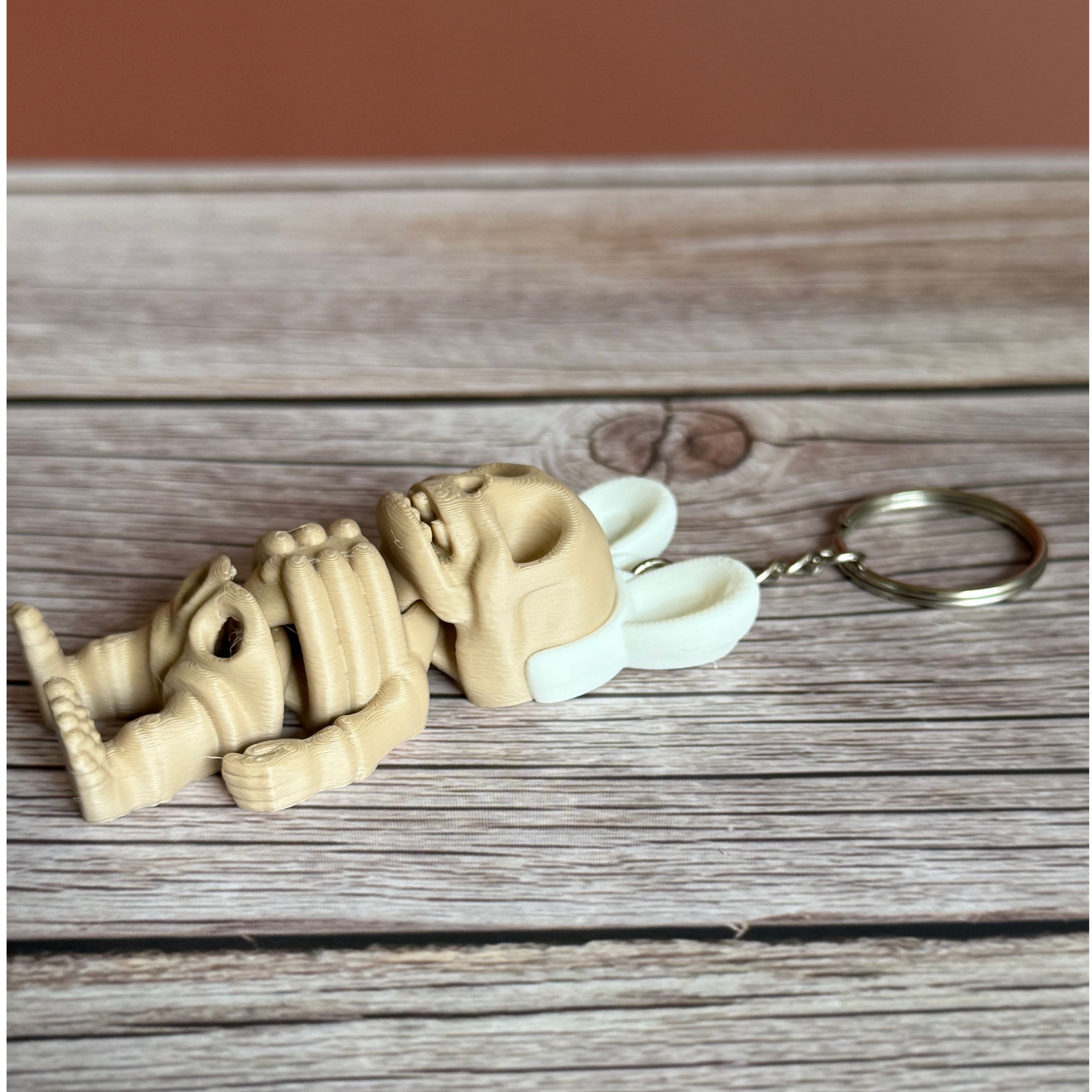 Side of a 3D printed keychain of a beige skeleton with white bunny ears on a wooden surface