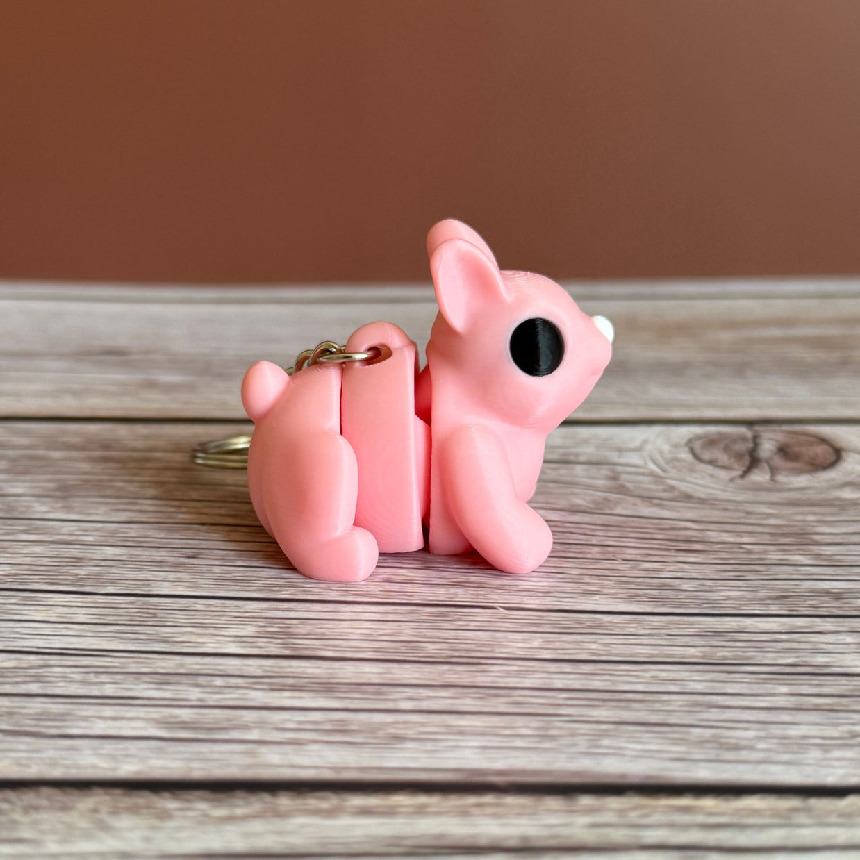 Side of a 3D printed pink bunny-shaped keychain on a wooden surface