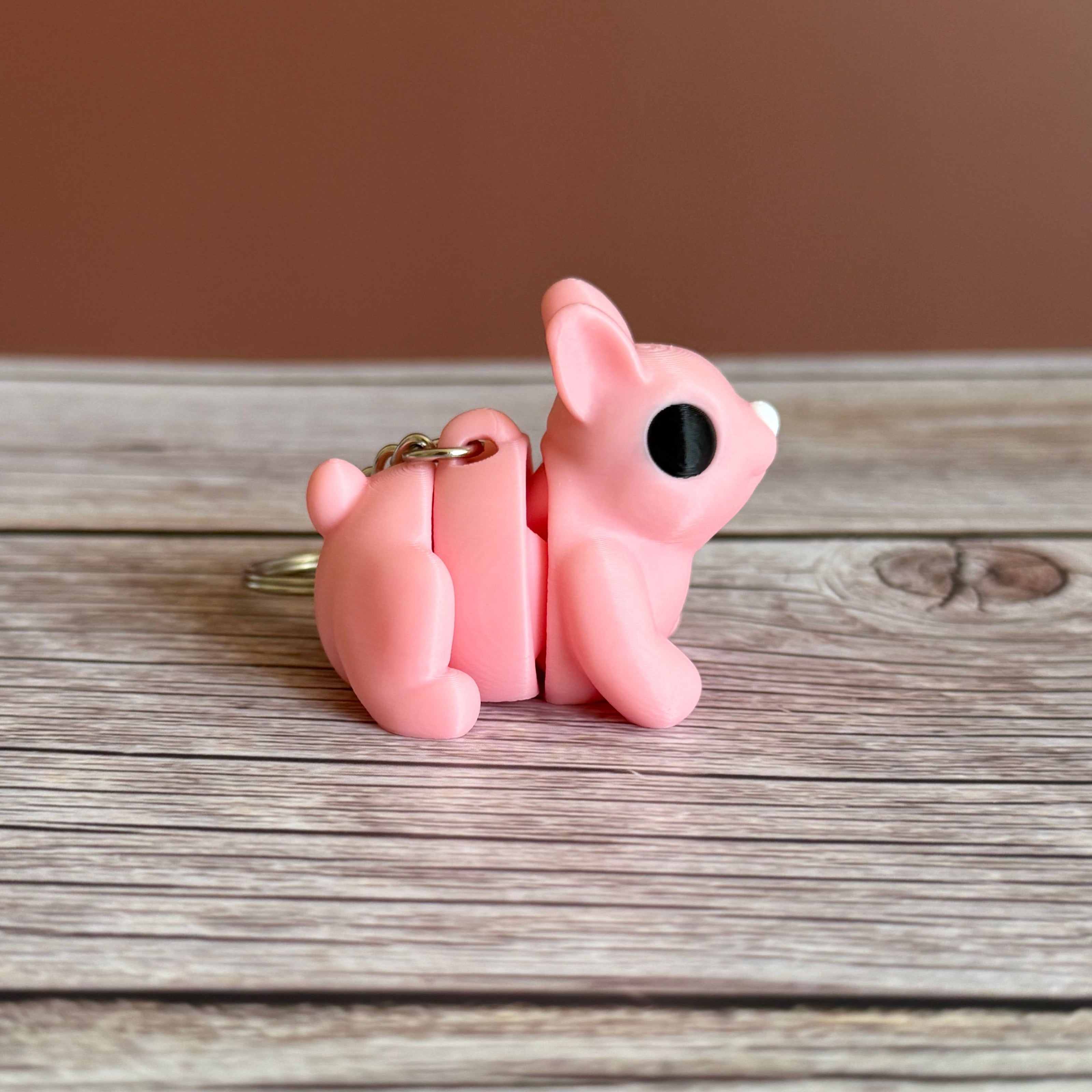 Side of a 3D printed pink bunny-shaped keychain on a wooden surface