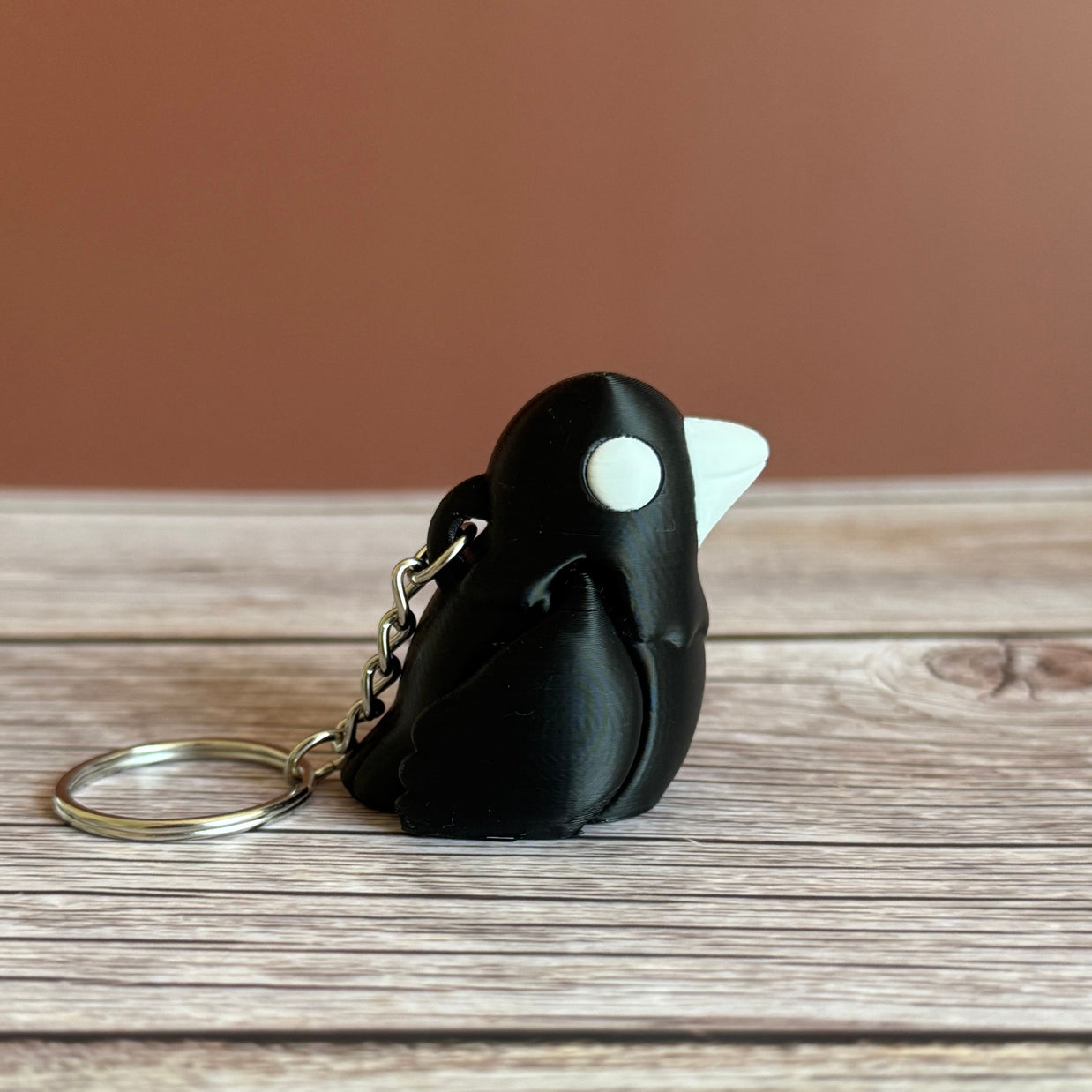 Side of a 3D printed black and white crow-shaped keychain on a wooden surface