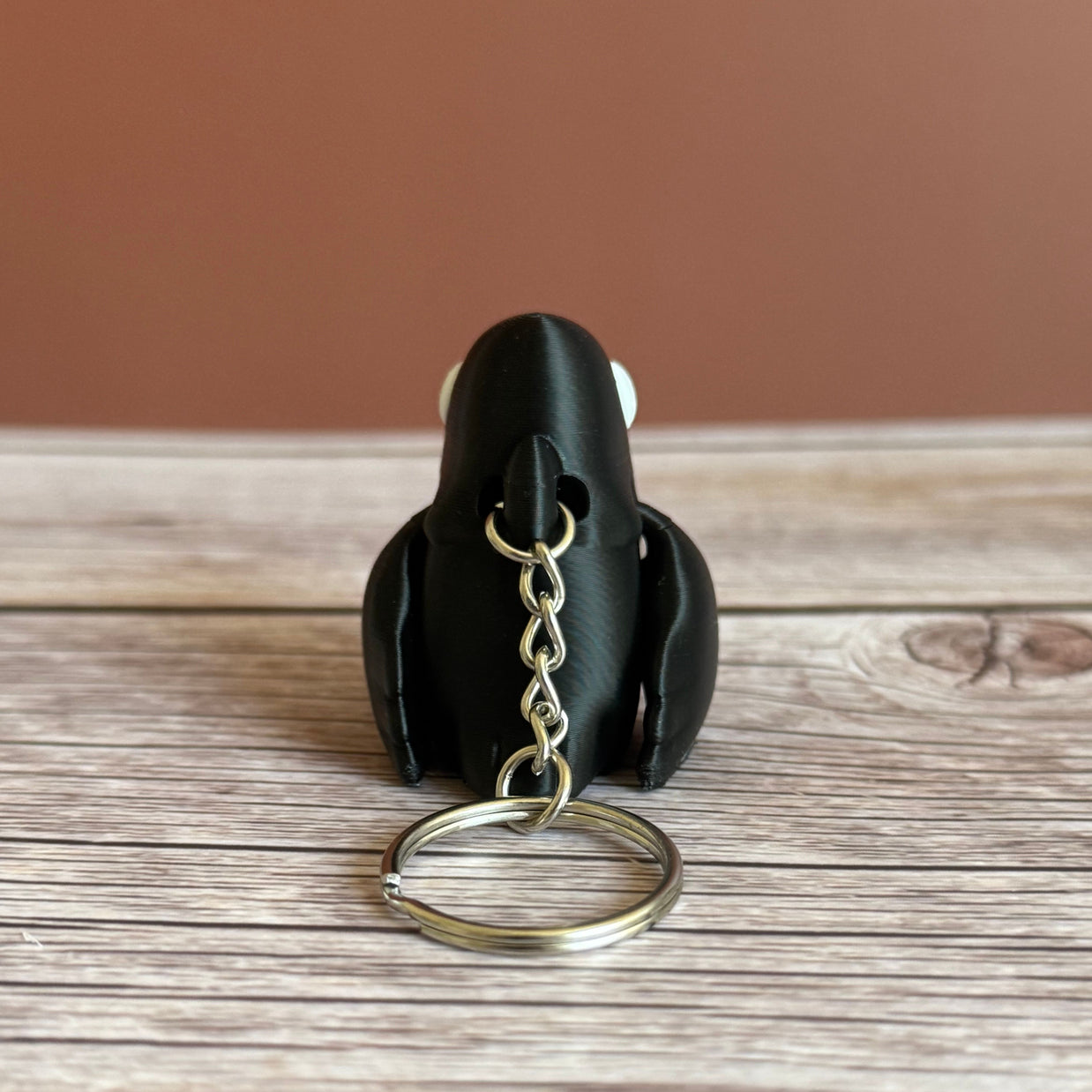 Back of a 3D printed black and white crow-shaped keychain on a wooden surface