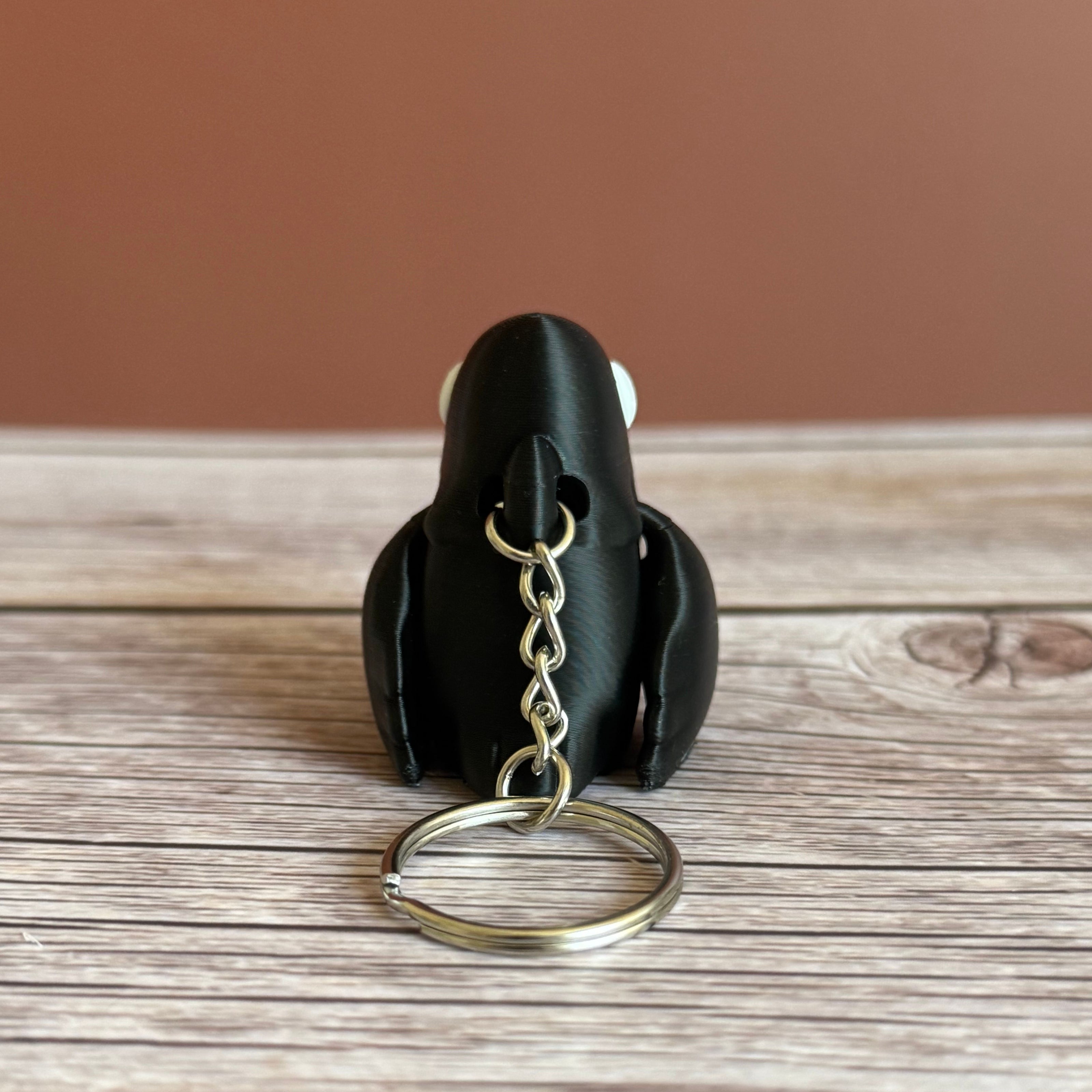 Back of a 3D printed black and white crow-shaped keychain on a wooden surface