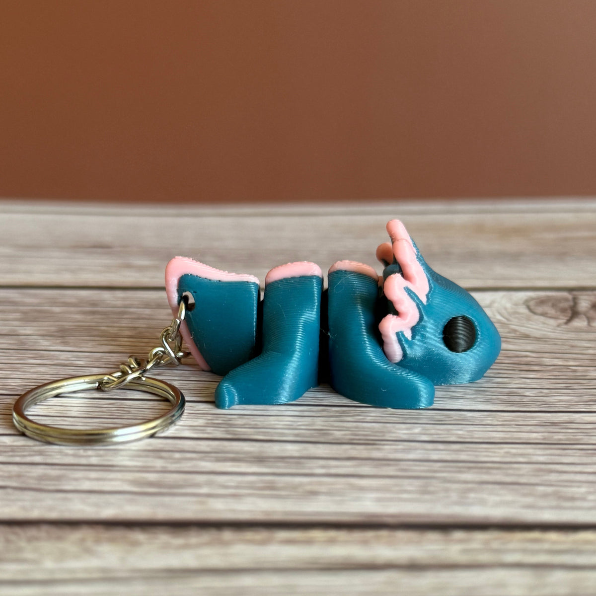 Side of a 3D printed blue and pink axolotl-shaped keychain on a wooden surface