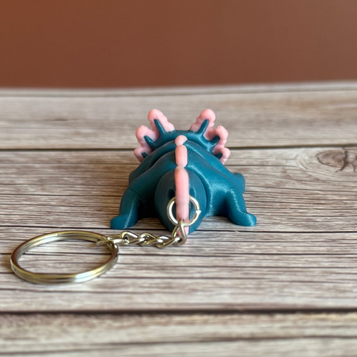 Back of a 3D printed blue and pink axolotl-shaped keychain on a wooden surface