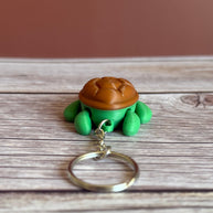 Back of a 3D printed turtle-shaped keychain with brown shell and green body on a wooden surface