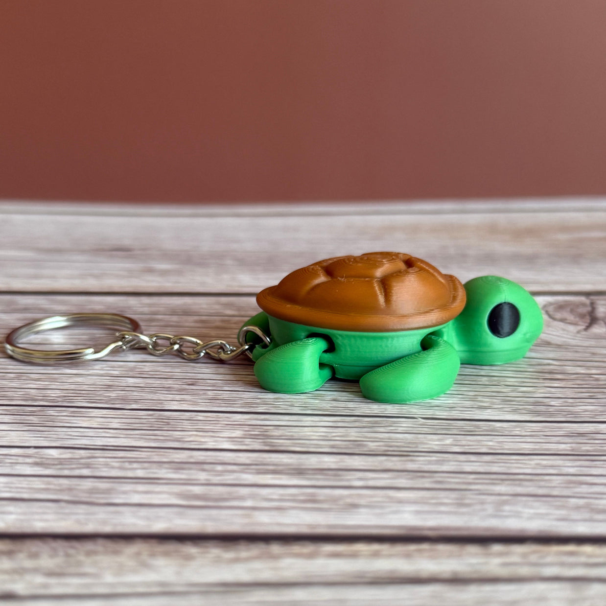 Side of a 3D printed turtle-shaped keychain with brown shell and green body on a wooden surface