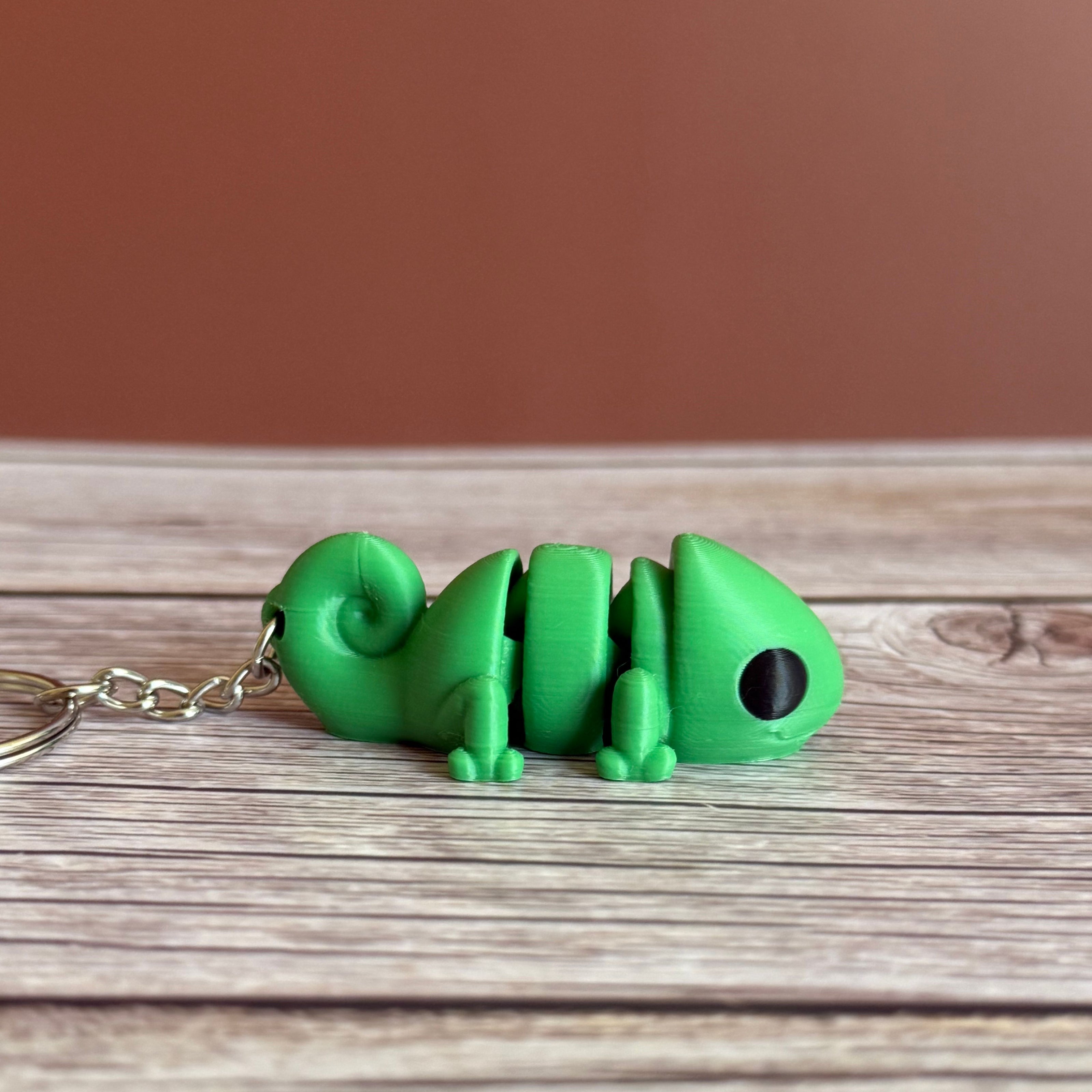 Side of a 3D printed green chameleon-shaped keychain on a wooden surface