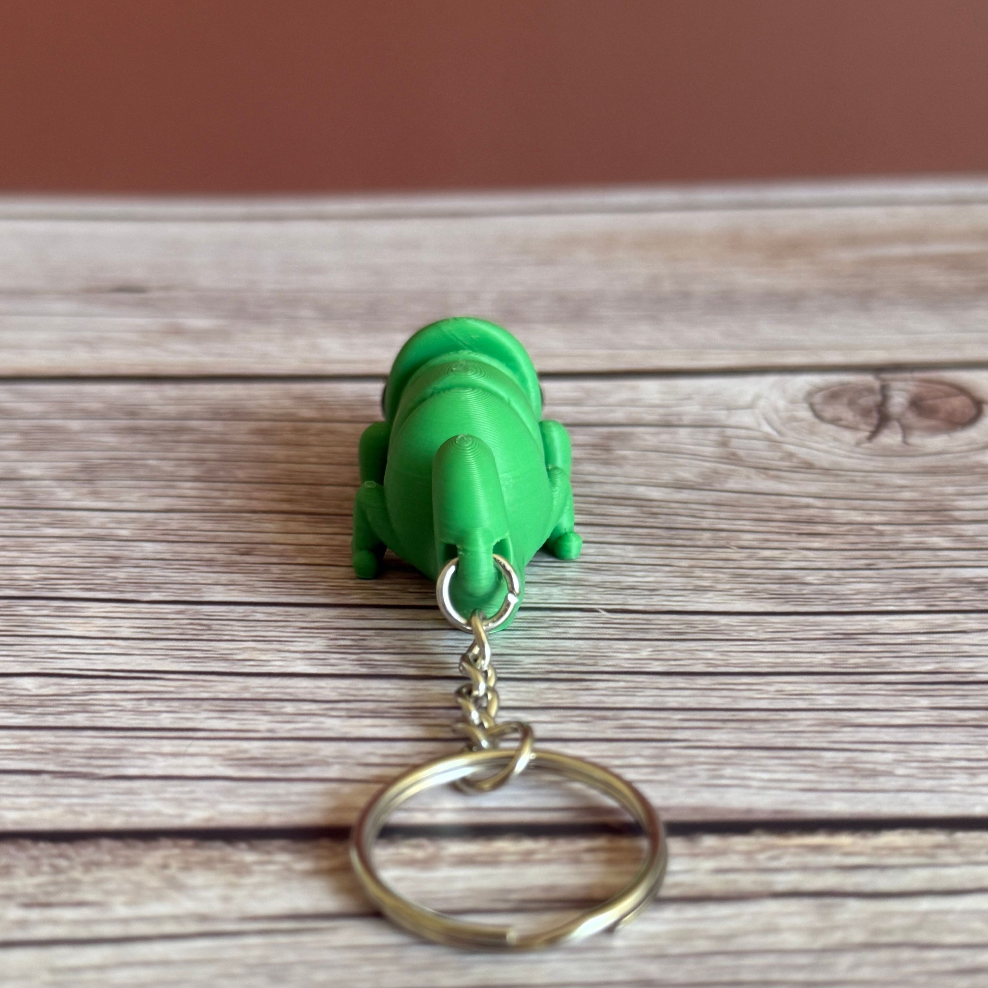 Back of a 3D printed green chameleon-shaped keychain on a wooden surface