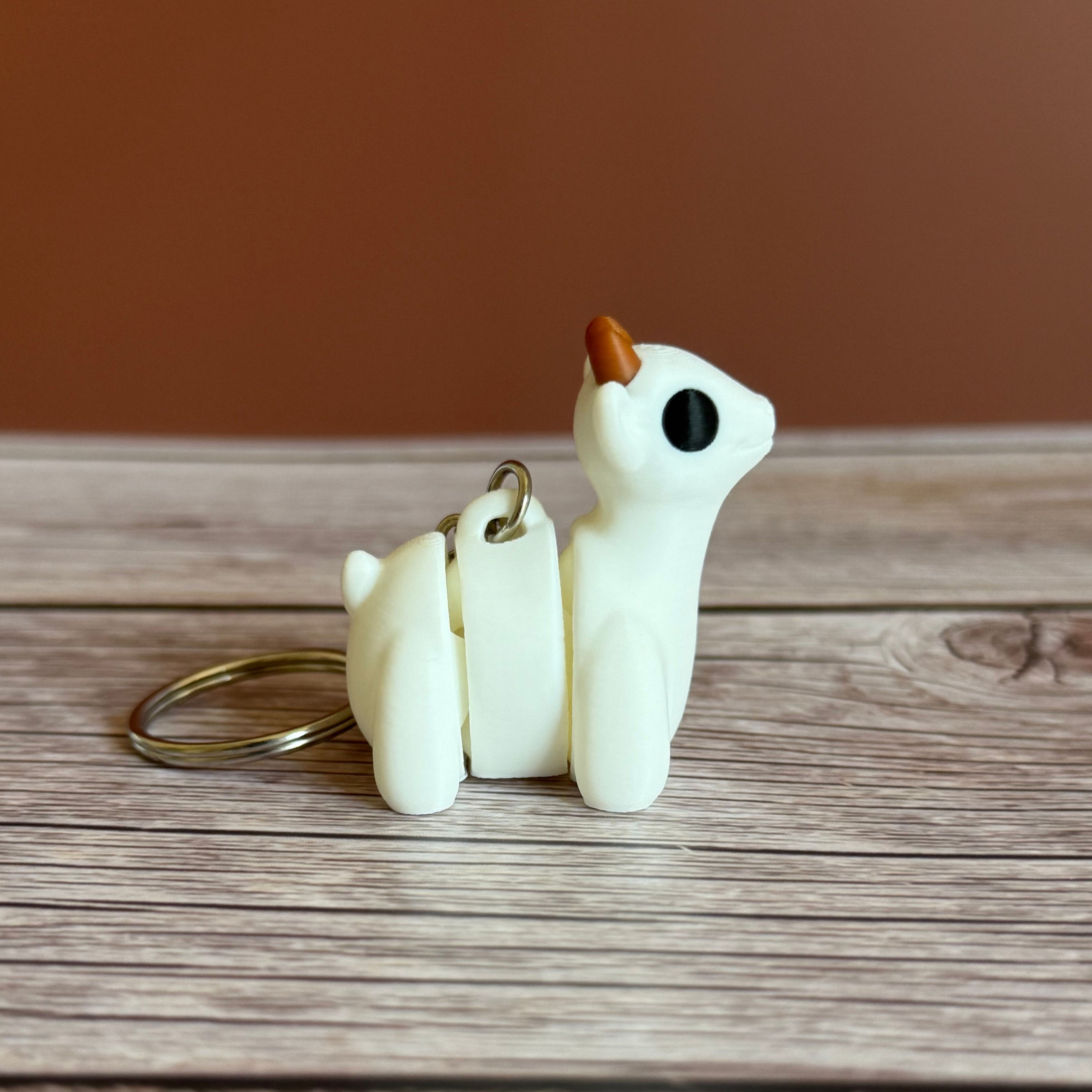 Side of a 3D printed white goat-shaped keychain with brown horns on a wooden surface
