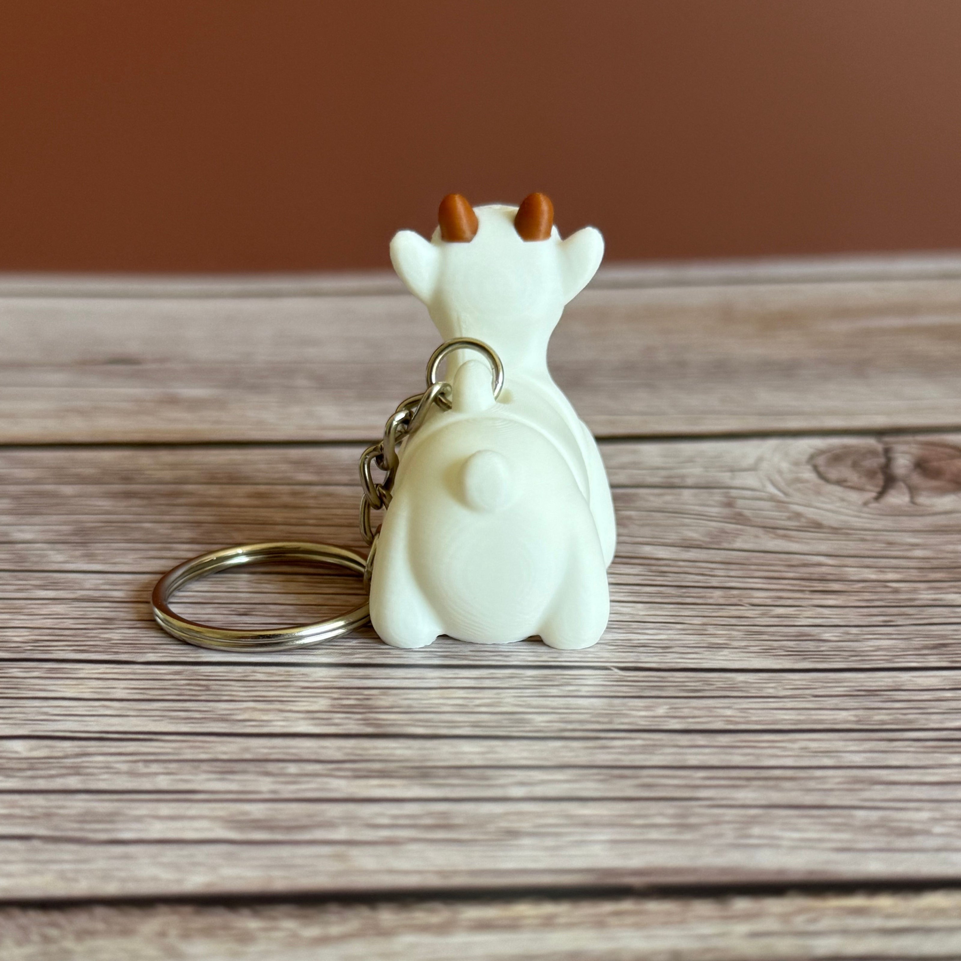 Back of a 3D printed white goat-shaped keychain with brown horns on a wooden surface