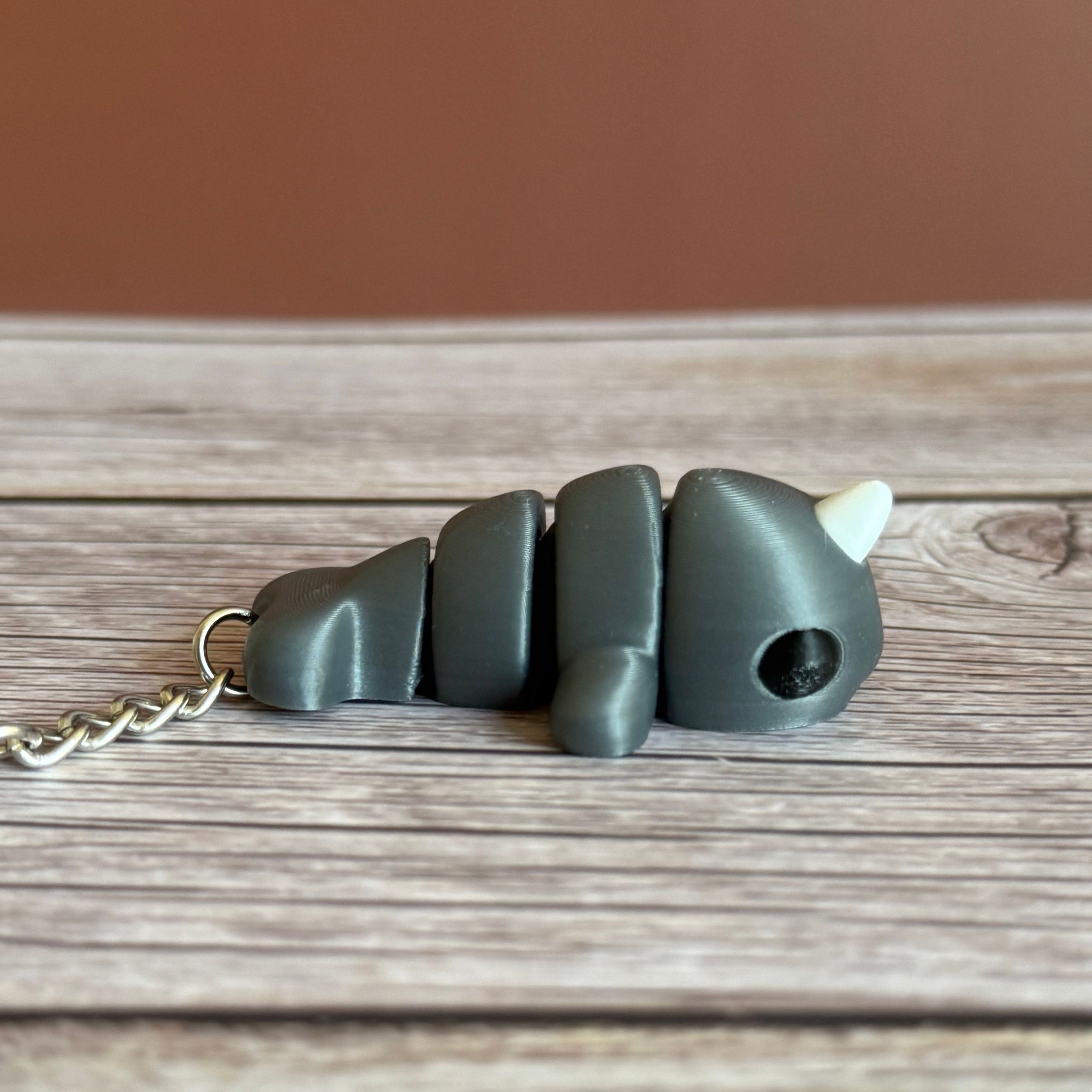 Side of a 3D printed gray narwhal-shaped keychain on a wooden surface
