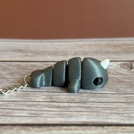 Side of a 3D printed gray narwhal-shaped keychain on a wooden surface