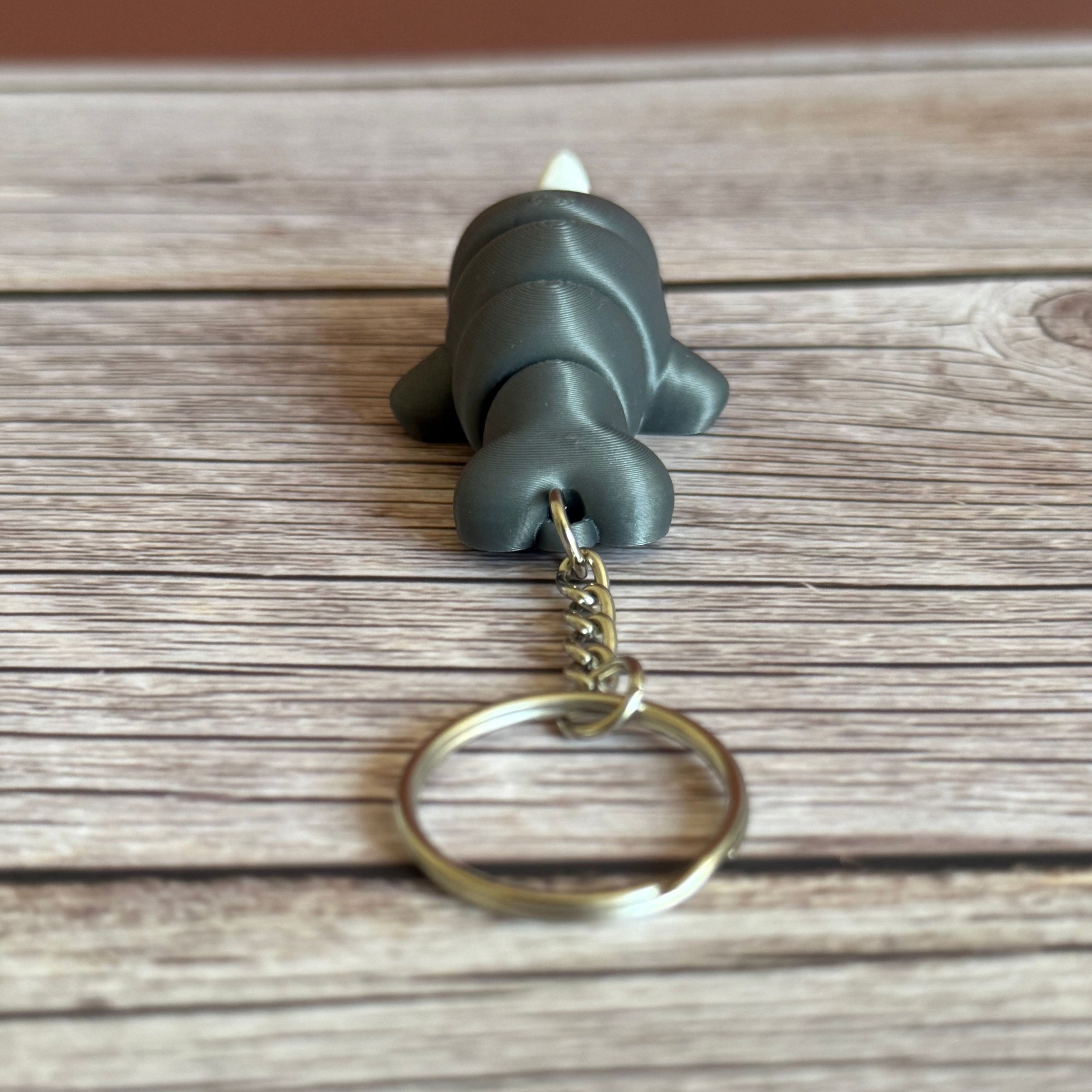 Back of a 3D printed gray narwhal-shaped keychain on a wooden surface