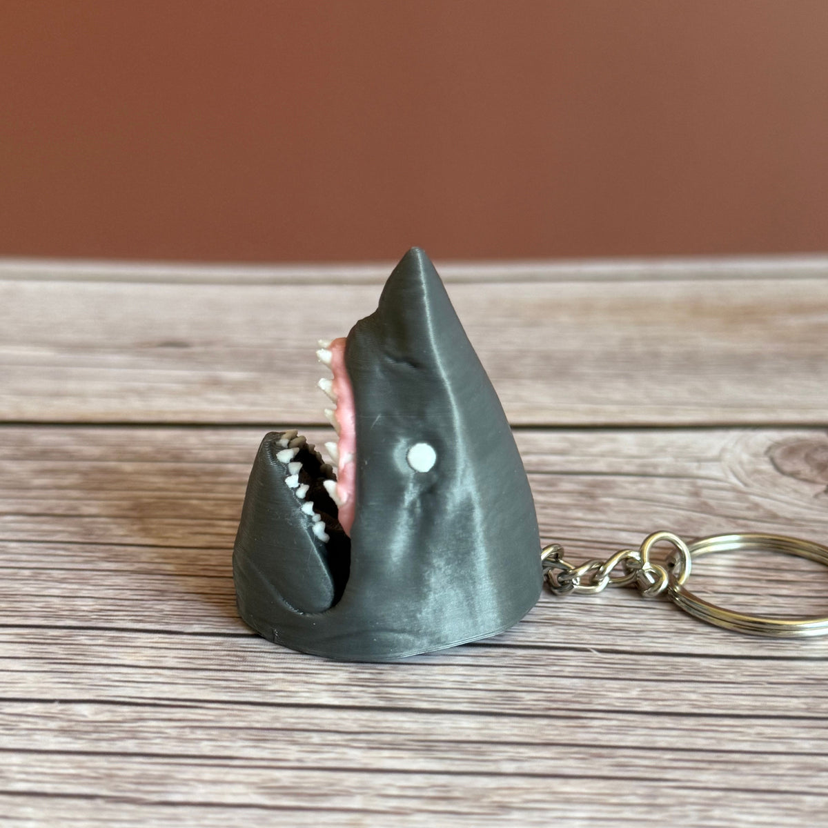 Side of a 3D printed gray keychain in the shape of a shark head with open mouth, set on a wooden surface
