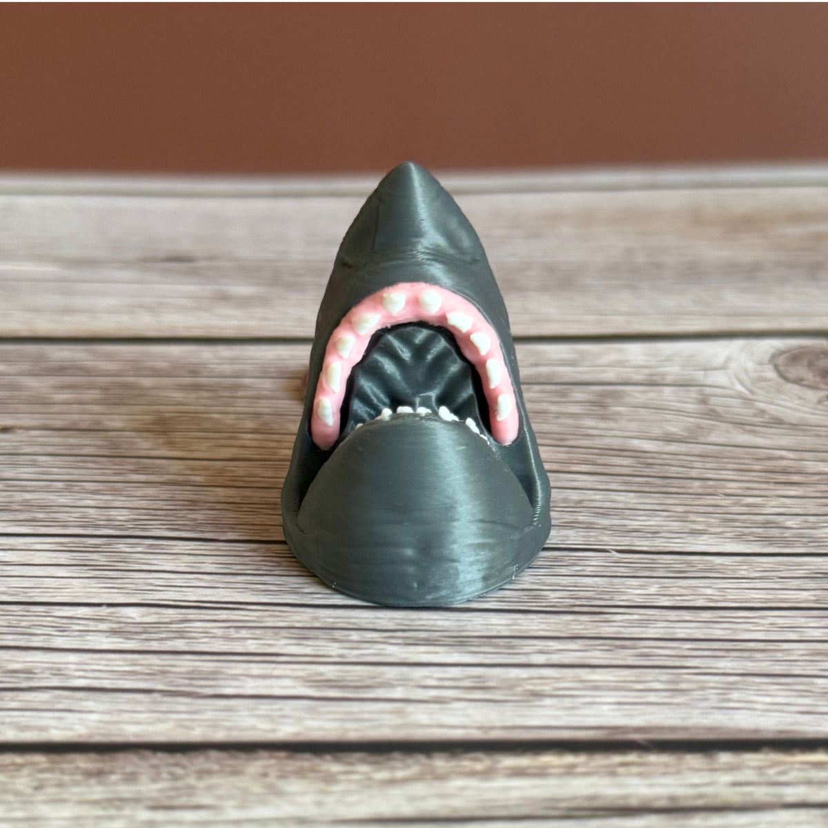 3D printed gray keychain in the shape of a shark head with open mouth, set on a wooden surface