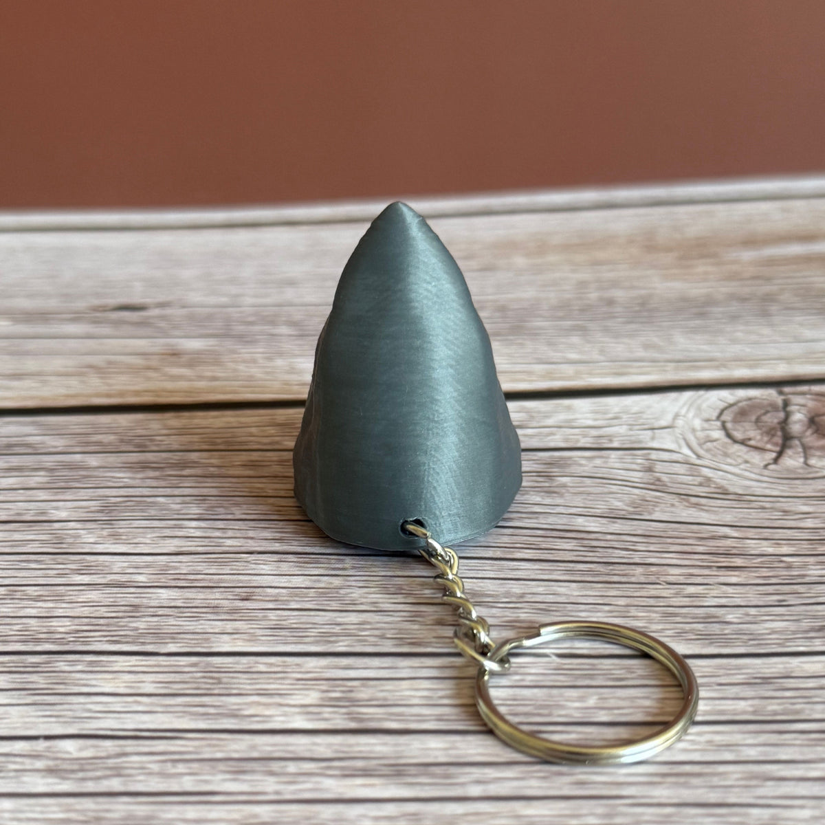 Top of a 3D printed gray keychain in the shape of a shark head, set on a wooden surface