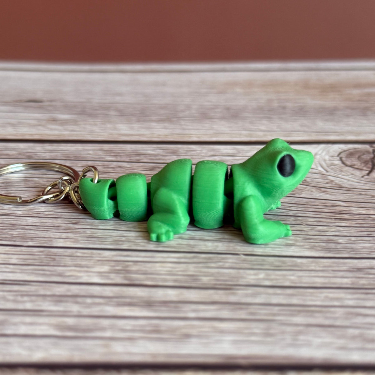 Side of a 3D printed green lizard-shaped keychain on a wooden surface