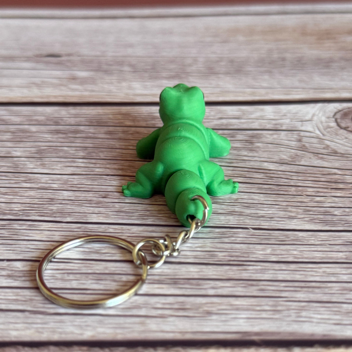 Back of a 3D printed green lizard-shaped keychain on a wooden surface