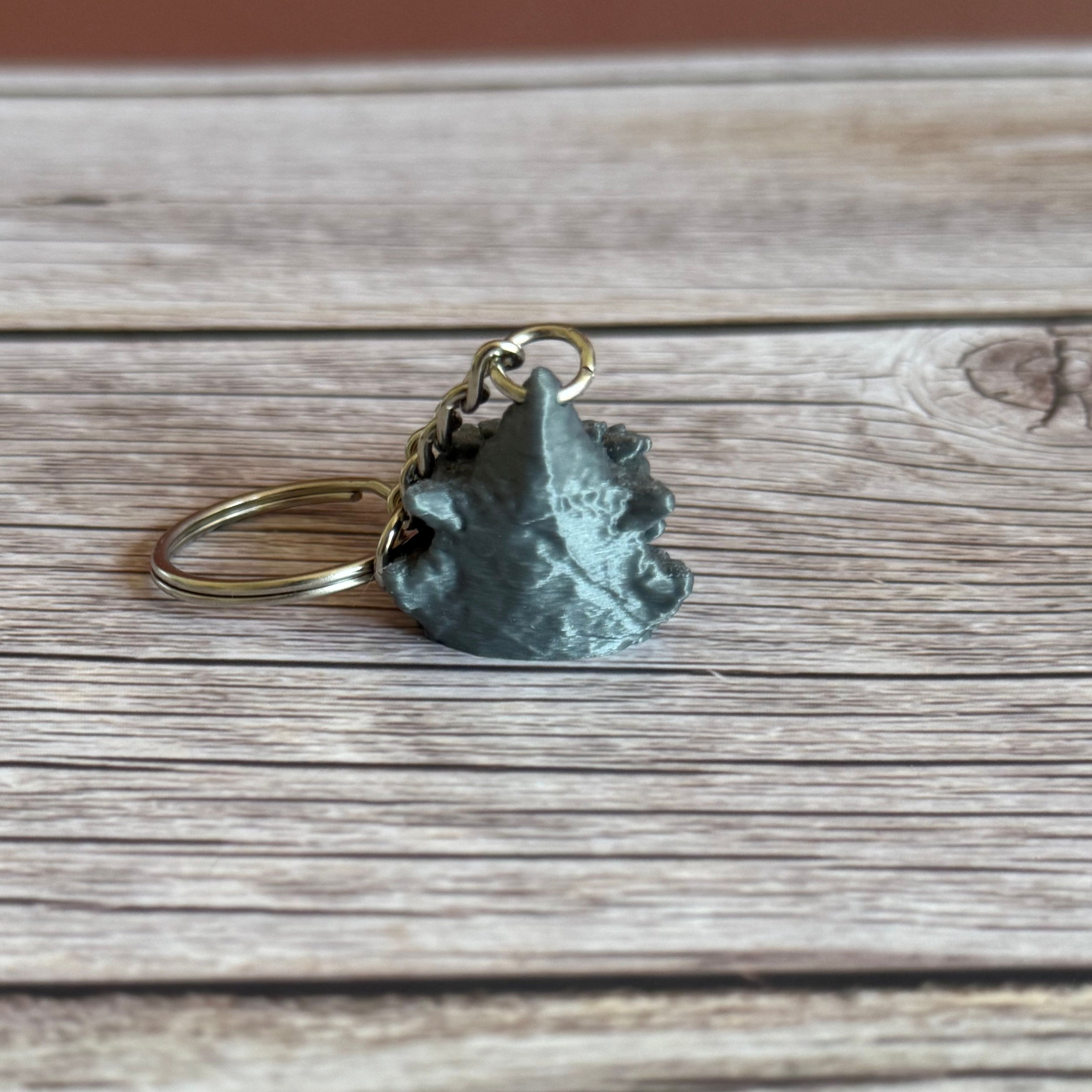 Back of a 3D printed gray dragon head keychain with blue eyes on a wooden surface