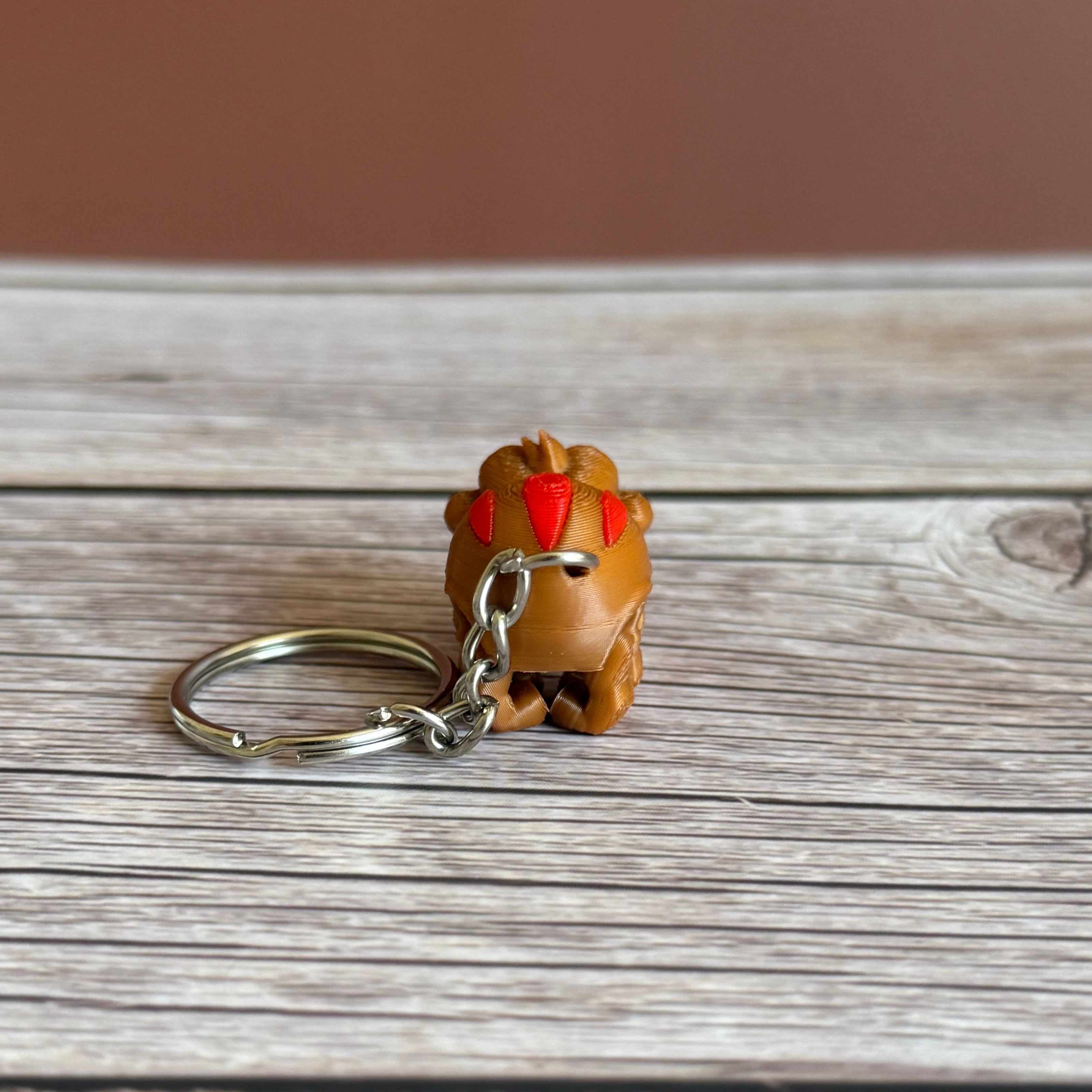 Back of a 3D printed brown and red tarantula-shaped keychain with legs curled under, placed on a wooden surface