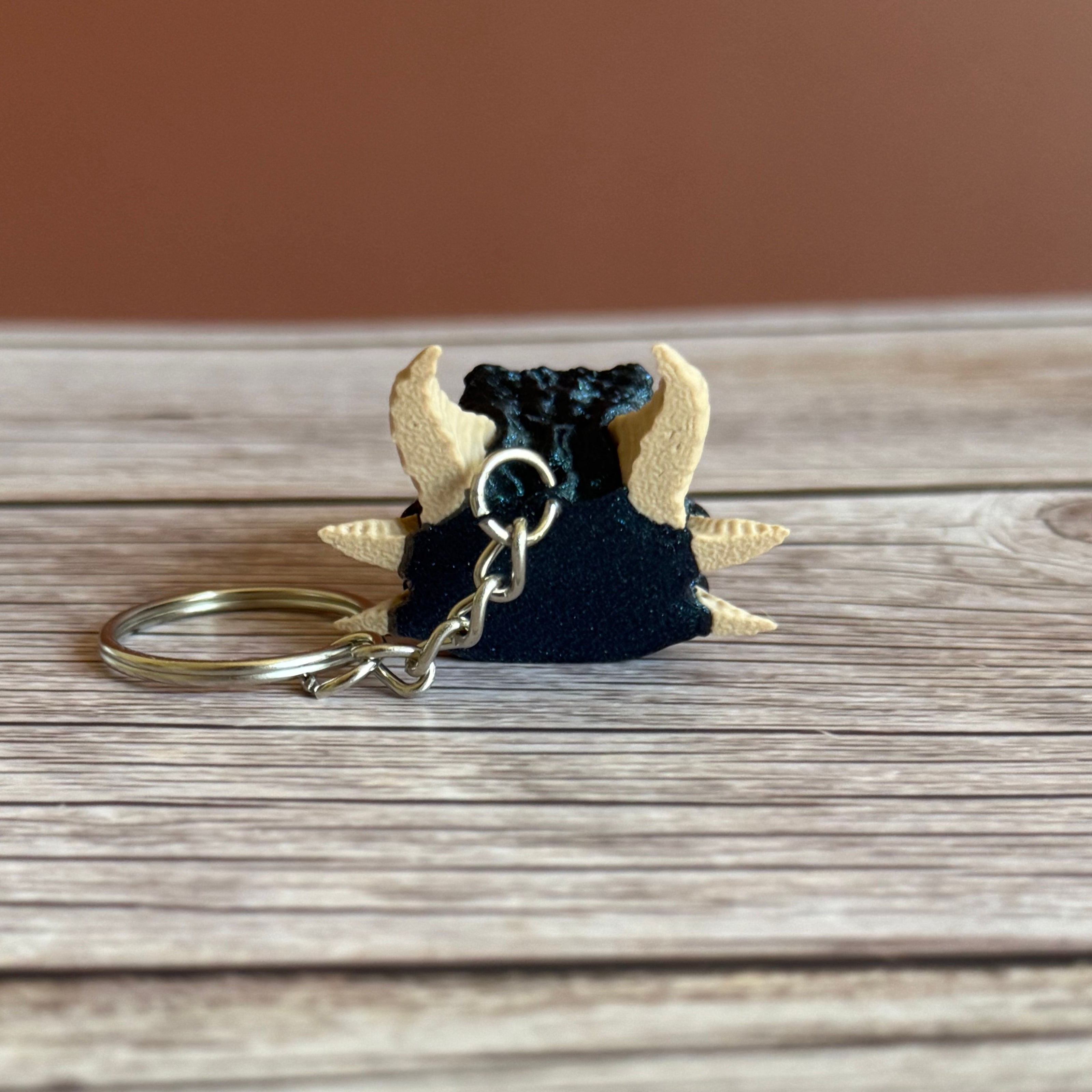 Back of a 3D printed blue dragon head keychain with beige horns on a wooden surface