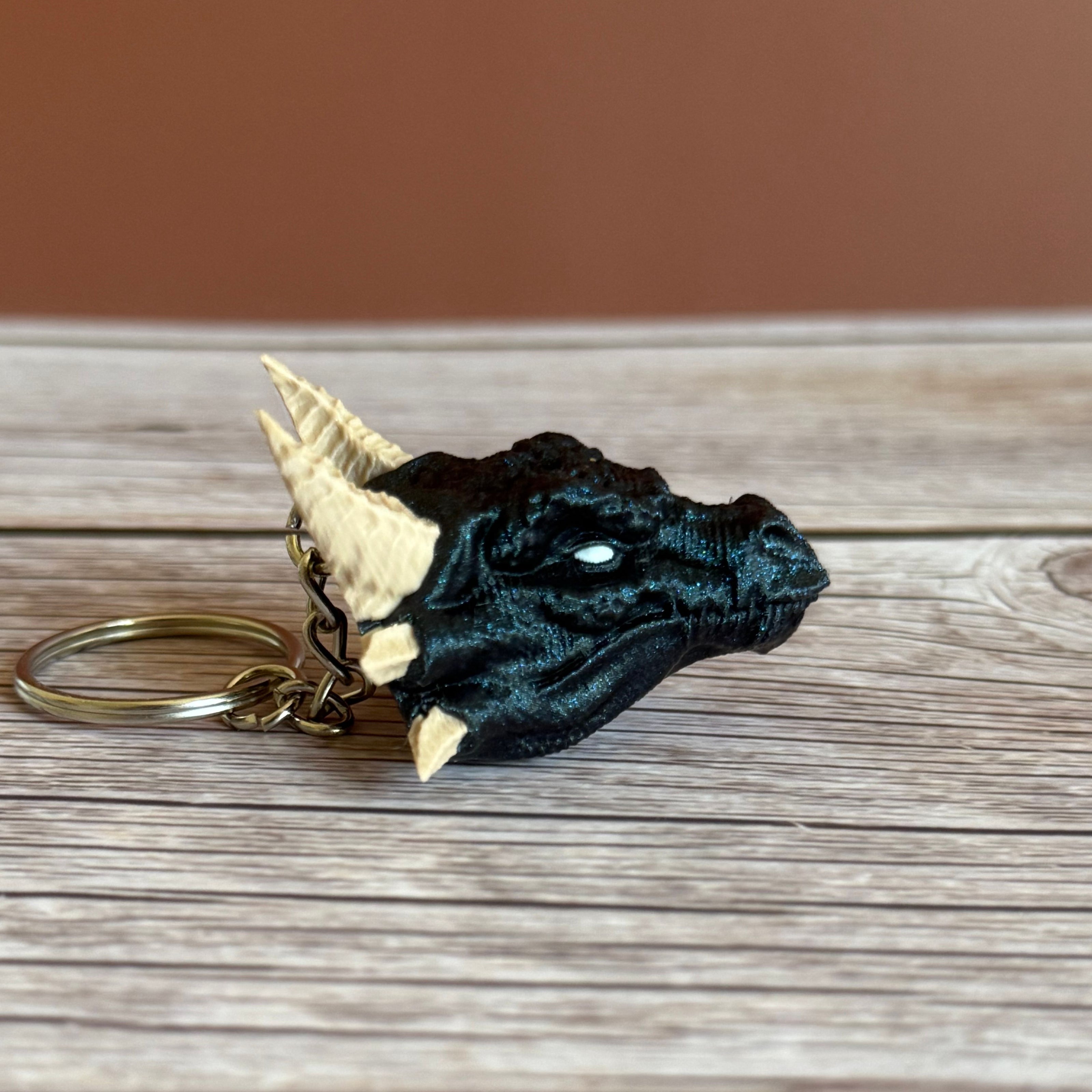 Side of a 3D printed blue dragon head keychain with beige horns on a wooden surface