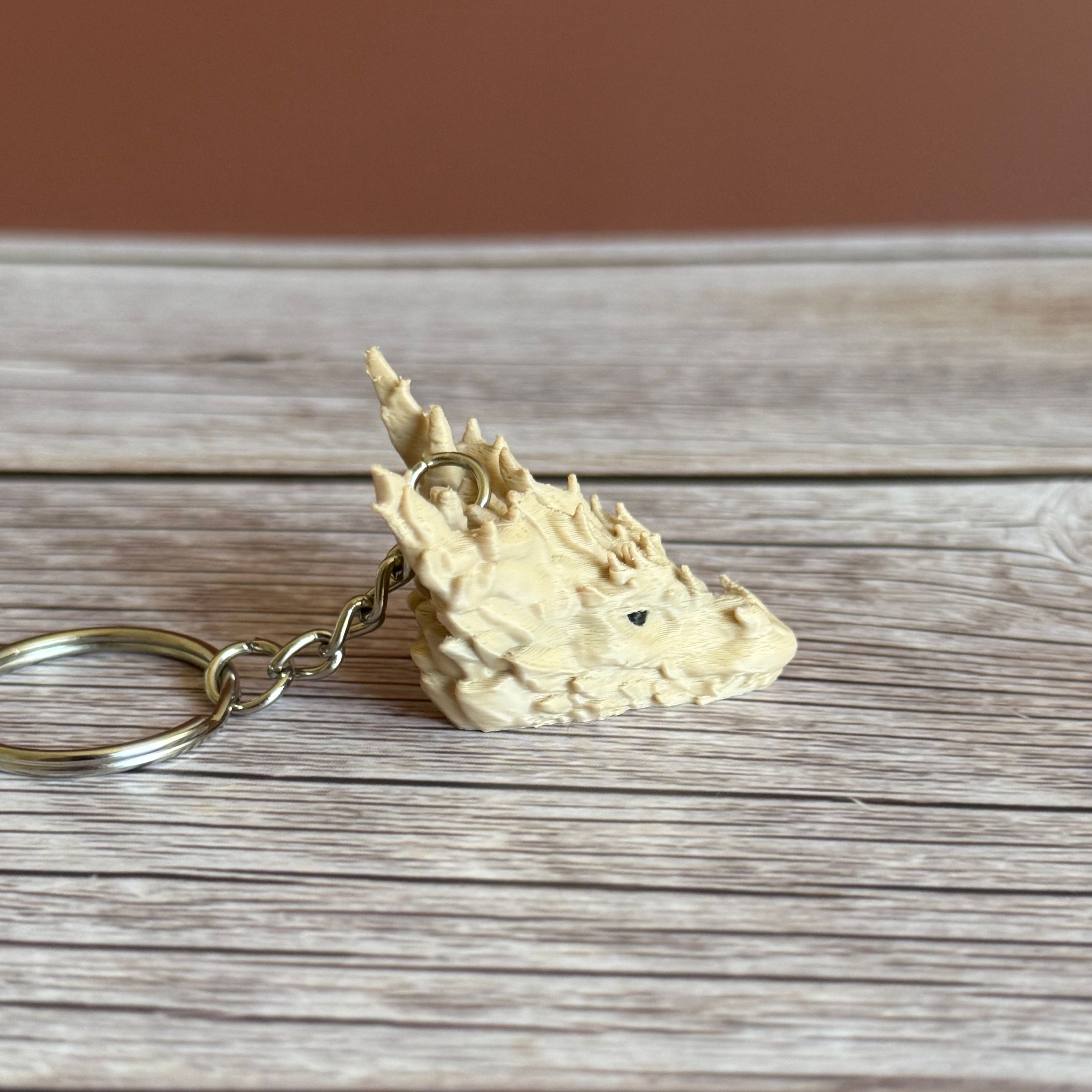 Side of a 3D printed beige dragon head keychain on a wooden surface