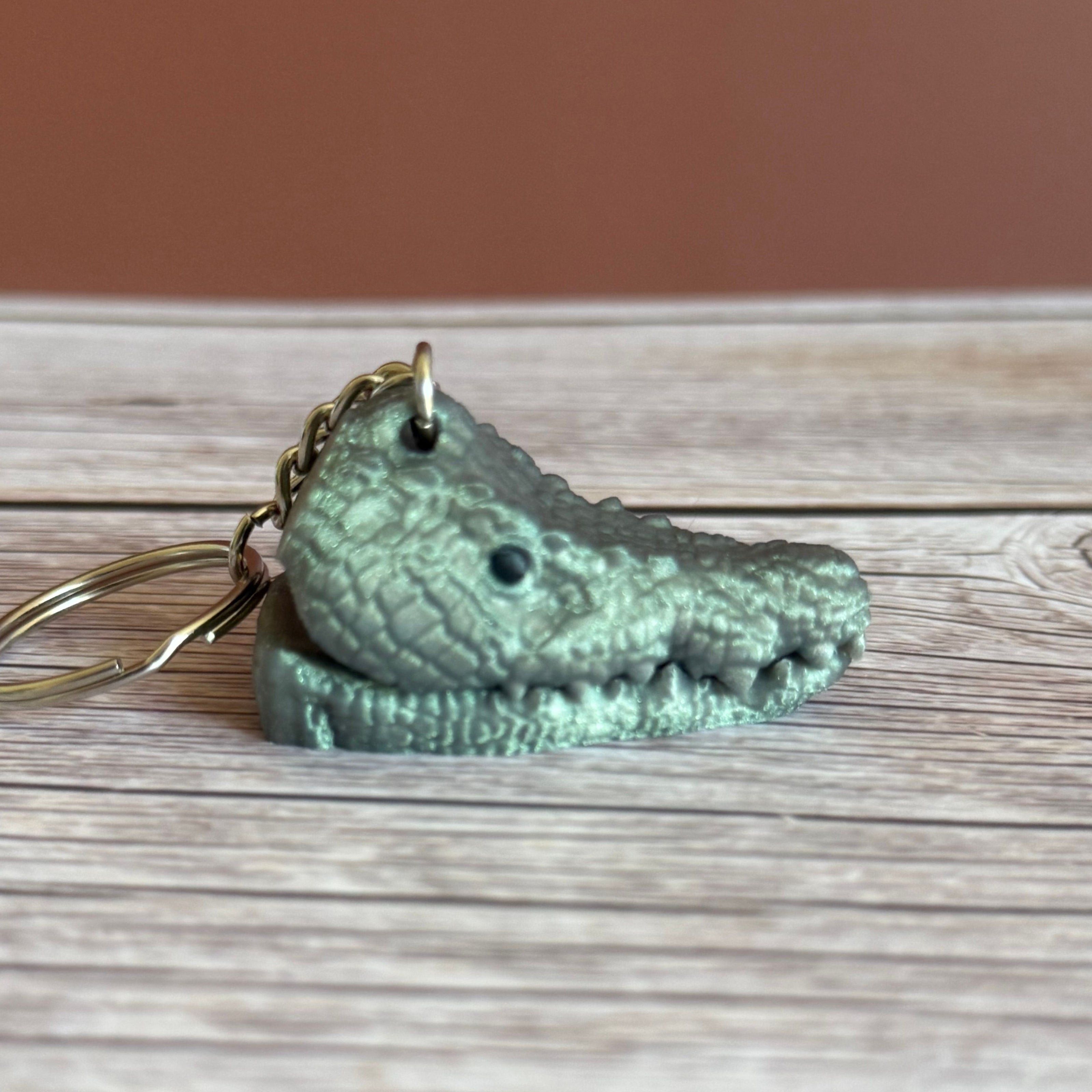 Side of a 3D printed shimmer green crocodile head-shaped keychain with a closed mouth on a wooden surface