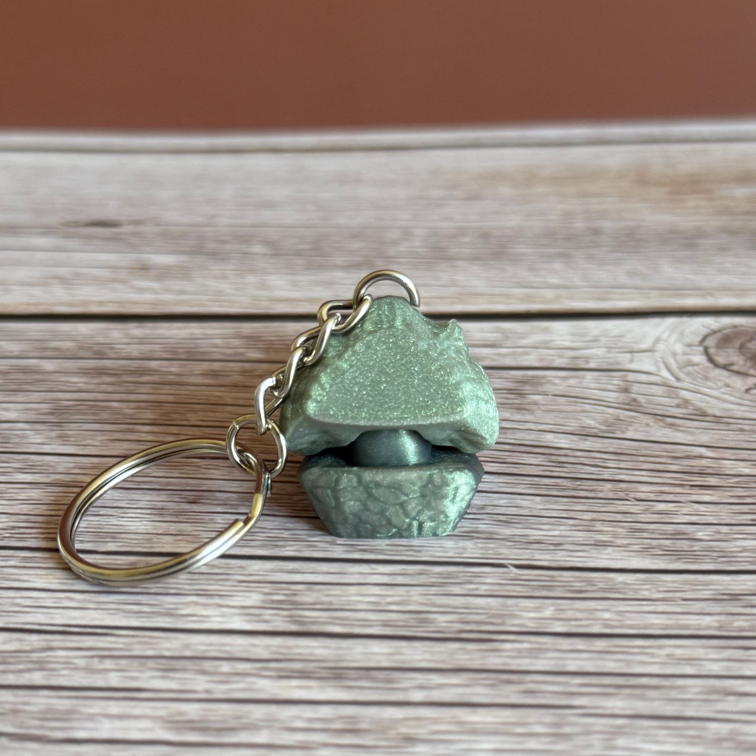 Back of a 3D printed shimmer green crocodile head-shaped keychain on a wooden surface
