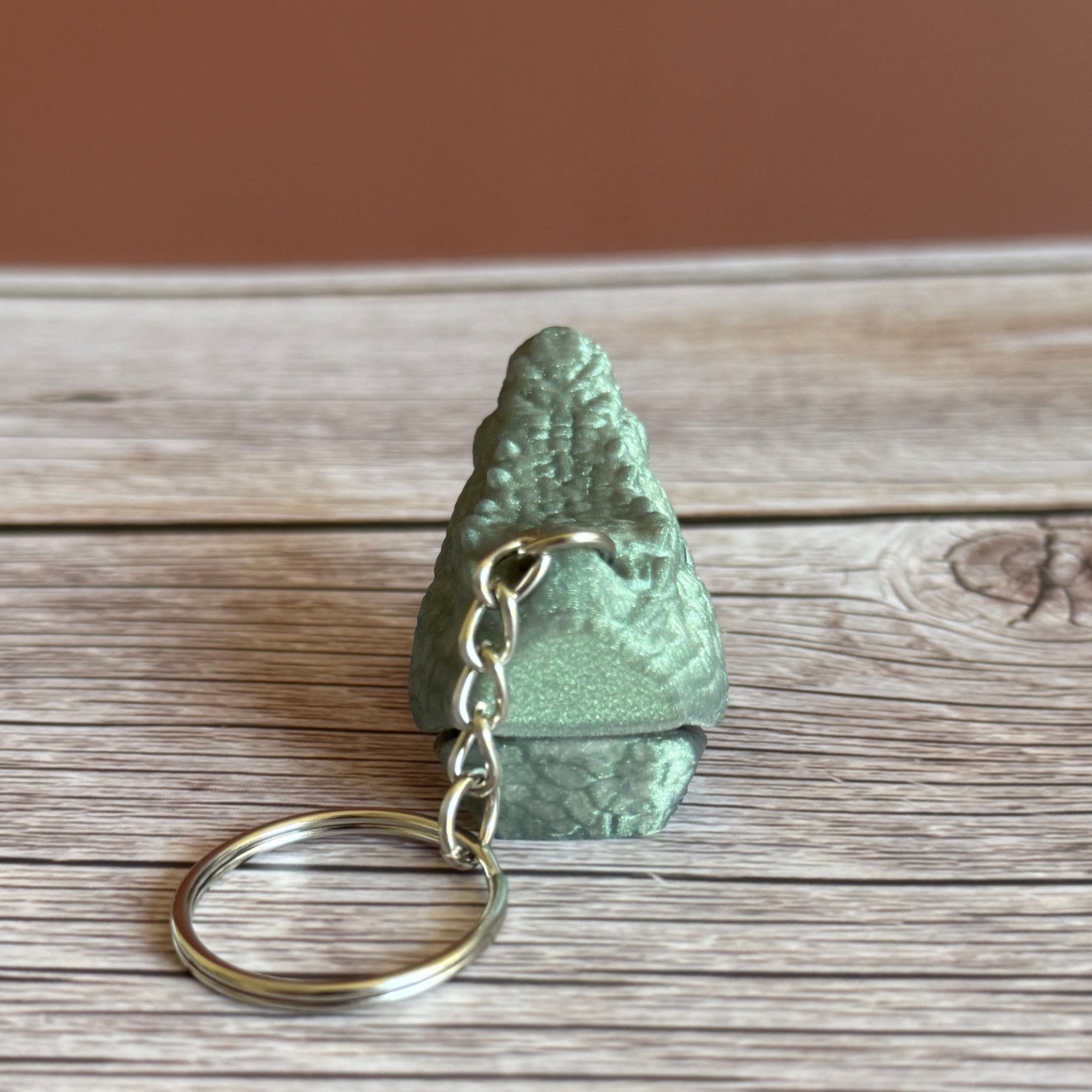 3D printed shimmer green crocodile head-shaped keychain with an open mouth on a wooden surface