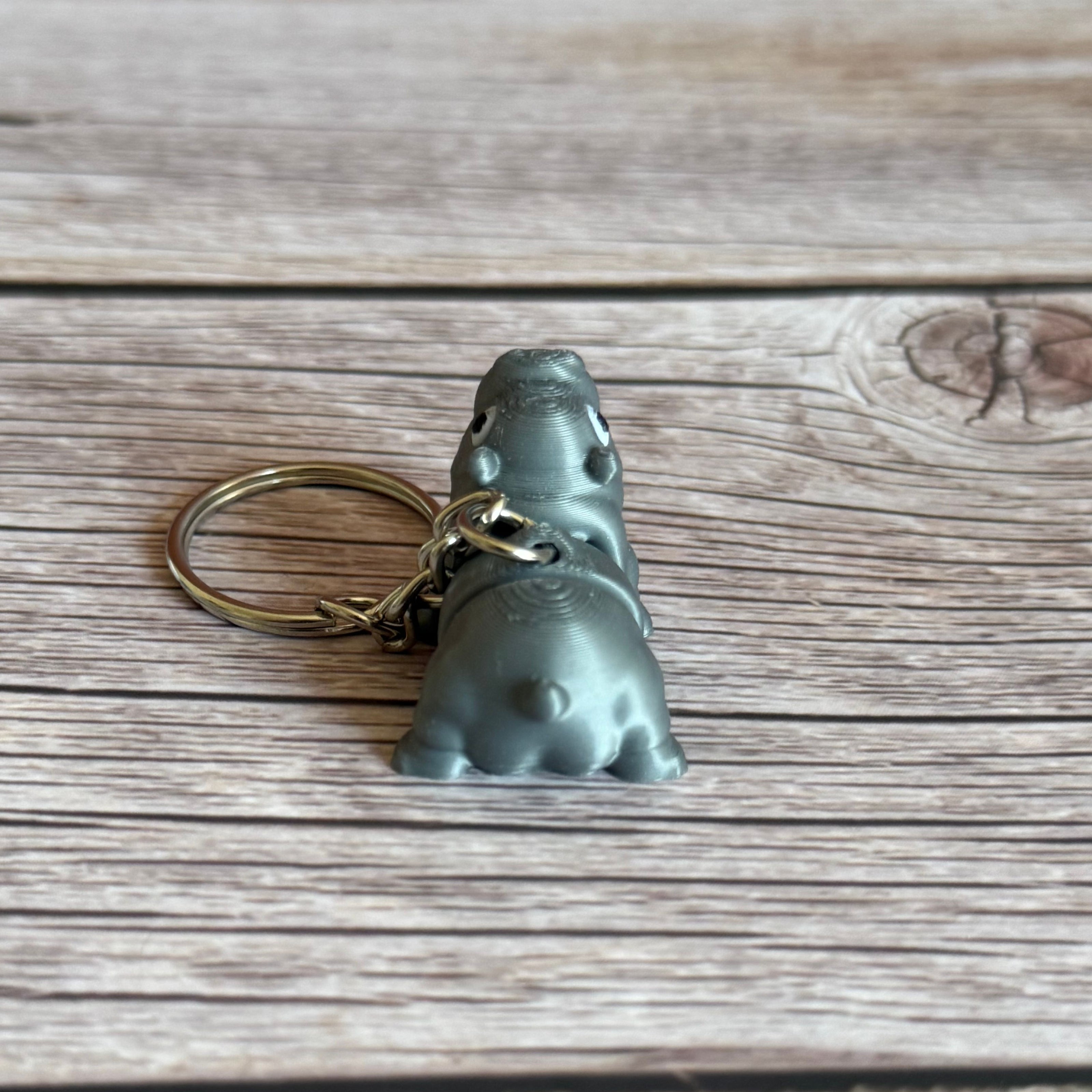 Back of a 3D printed gray and pink hippo-shaped keychain on a wooden surface