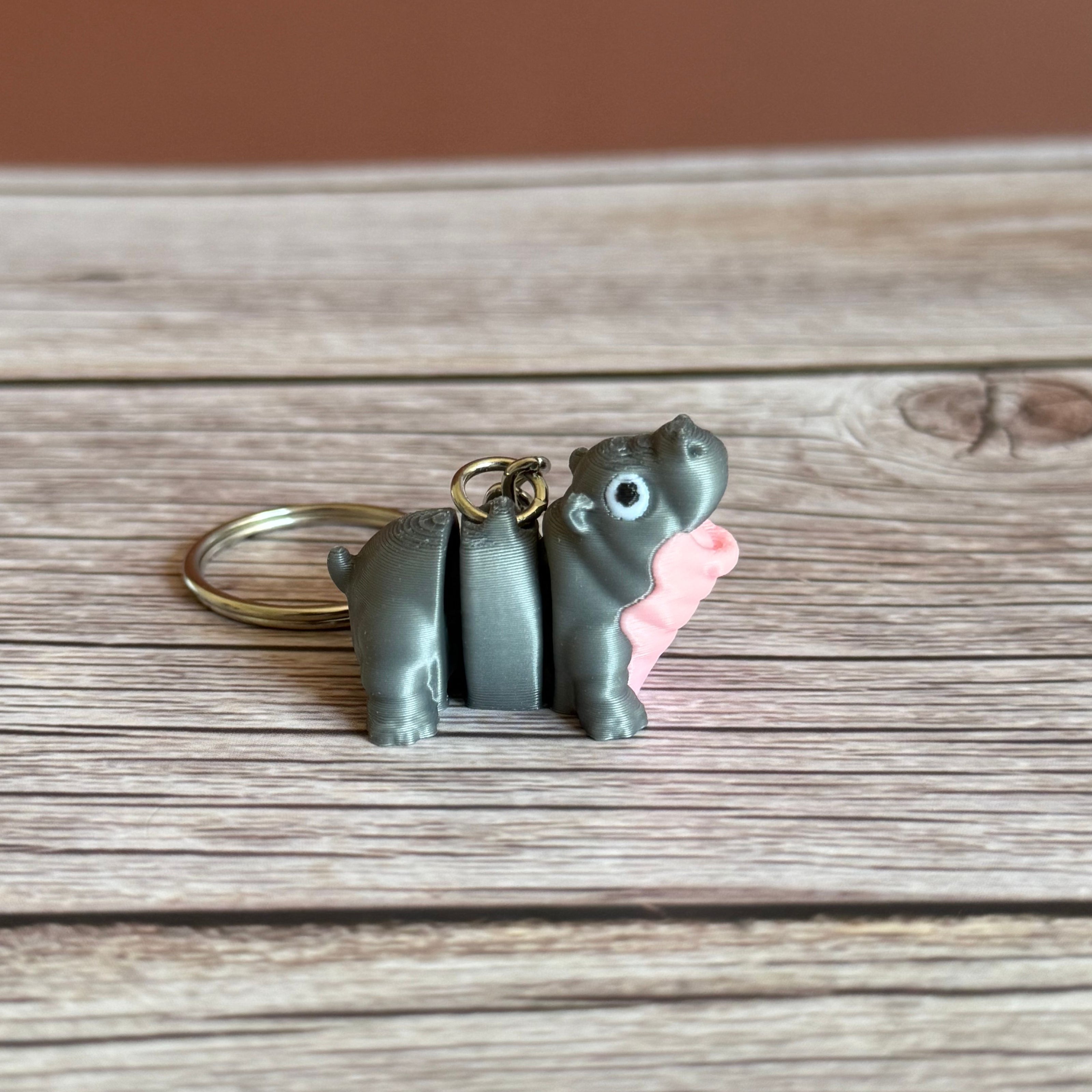 Side of a 3D printed gray and pink hippo-shaped keychain on a wooden surface