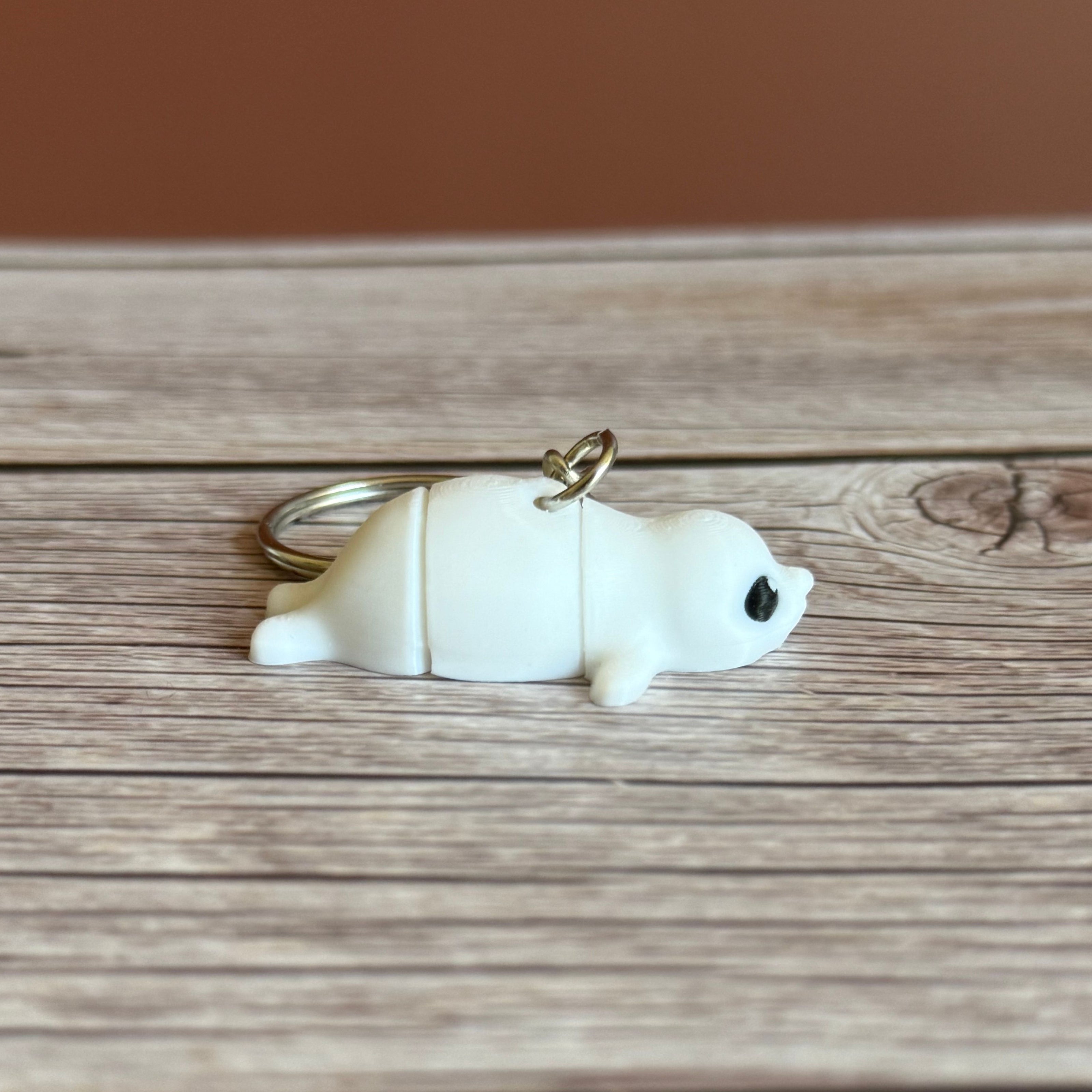 Side of a 3D printed white seal-shaped keychain on a wooden surface
