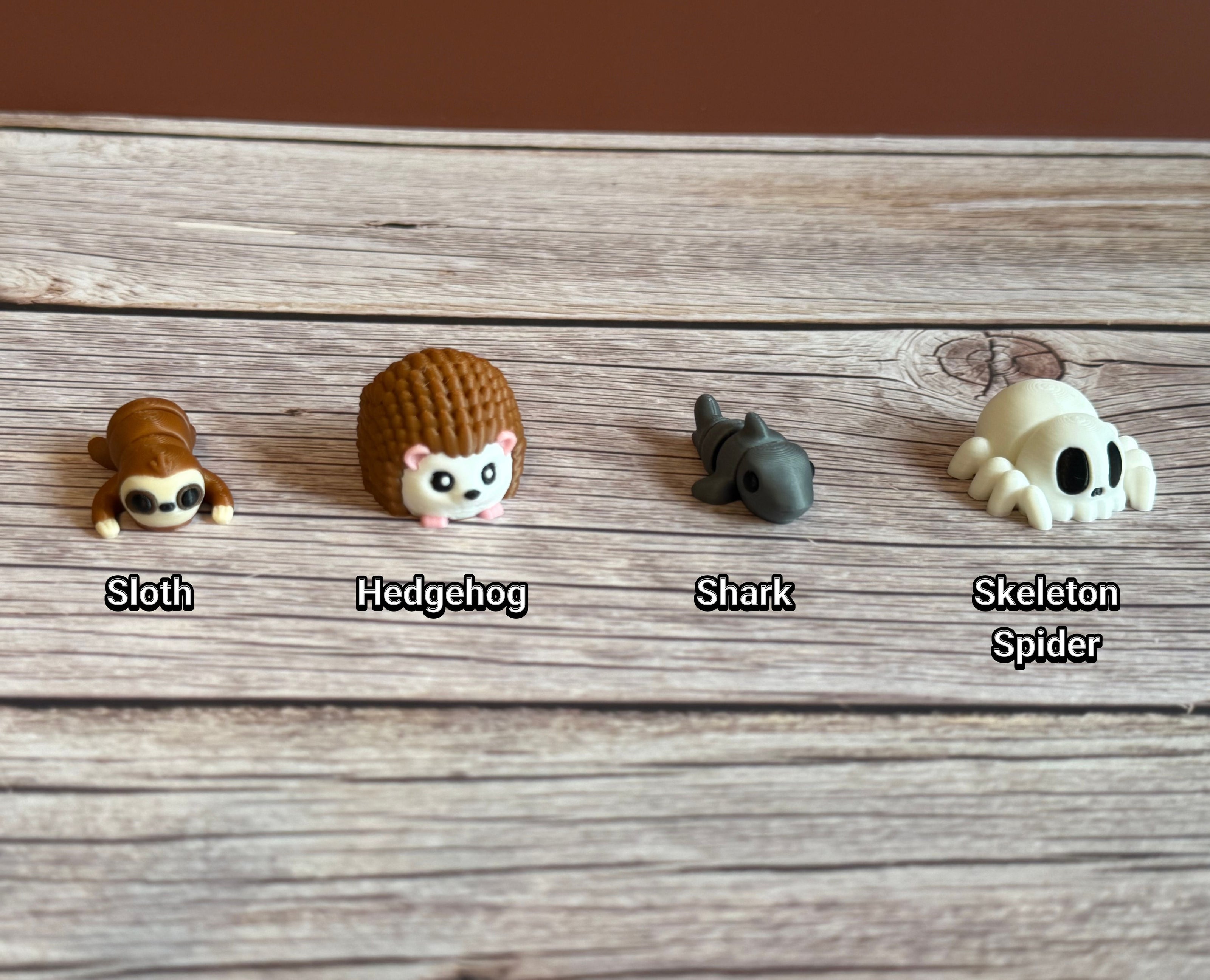 Collection of small animal figurines on a wooden surface. Hedgehog, sloth, shark, and spider-shaped skeleton are featured. 