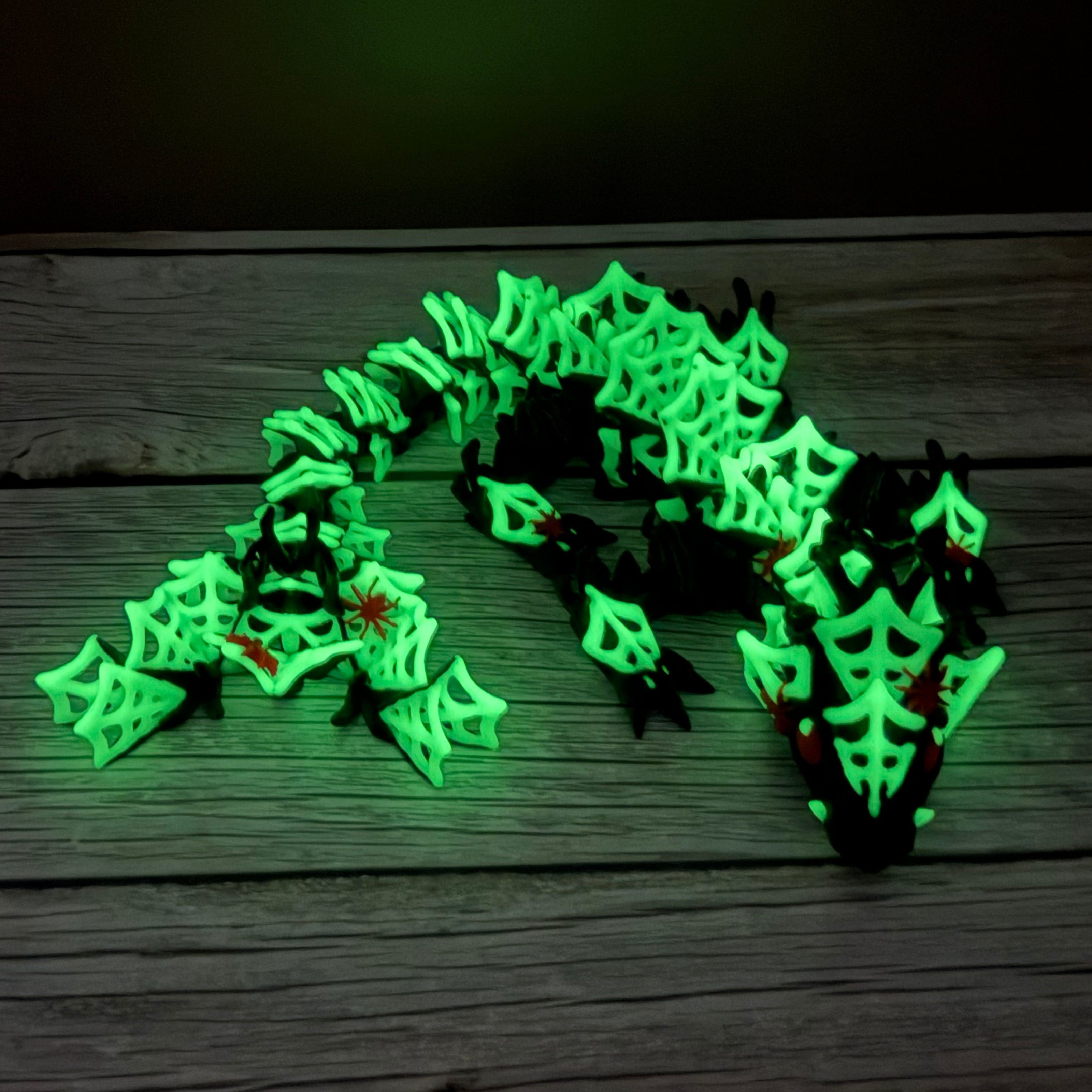 3D printed black dragon with glow in the dark spider webs and red spiders across the body, placed on a wooden surface with a brown backdrop