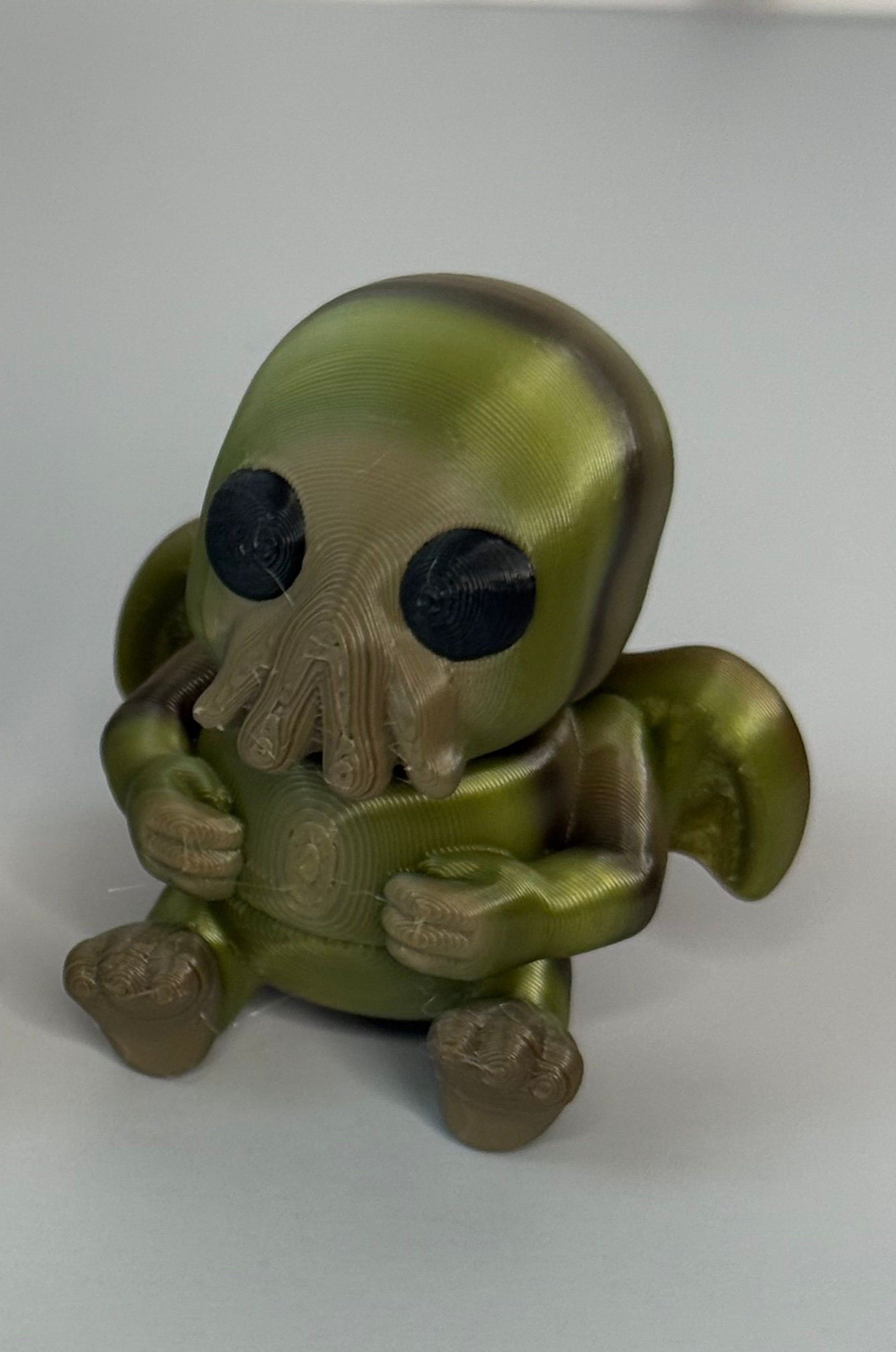 Sitting Cthulhu-shaped figure with wings and face-tentacles on a gray background