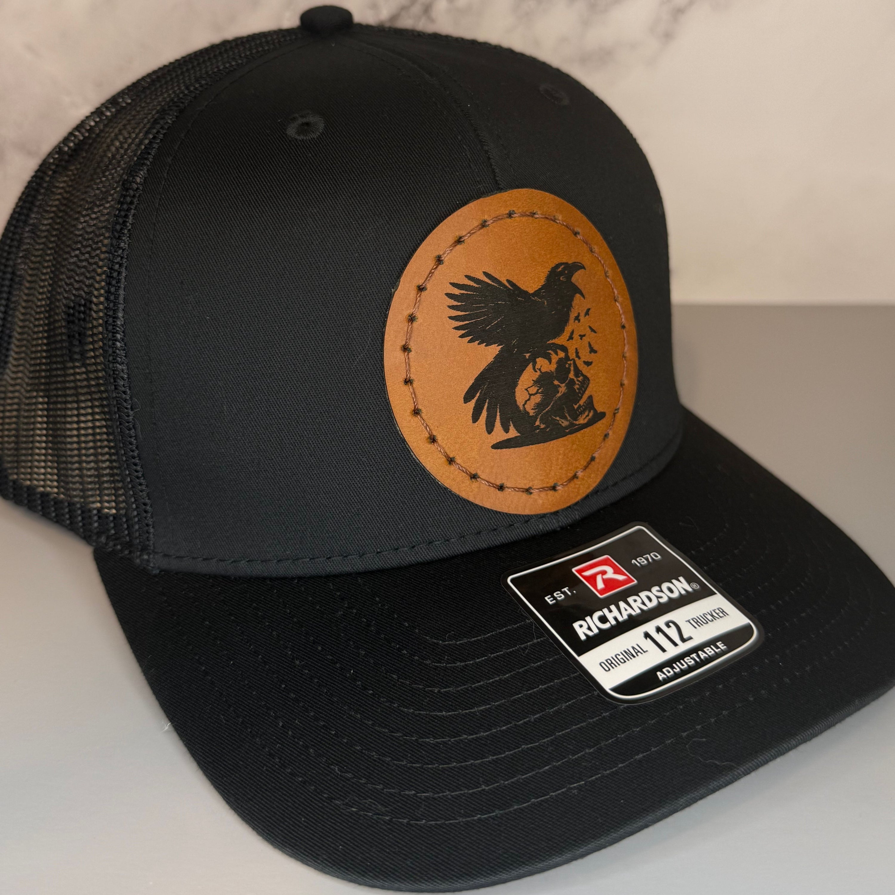 Black cap with a Richardson sticker and a brown leather patch featuring skull and raven design on a gray background