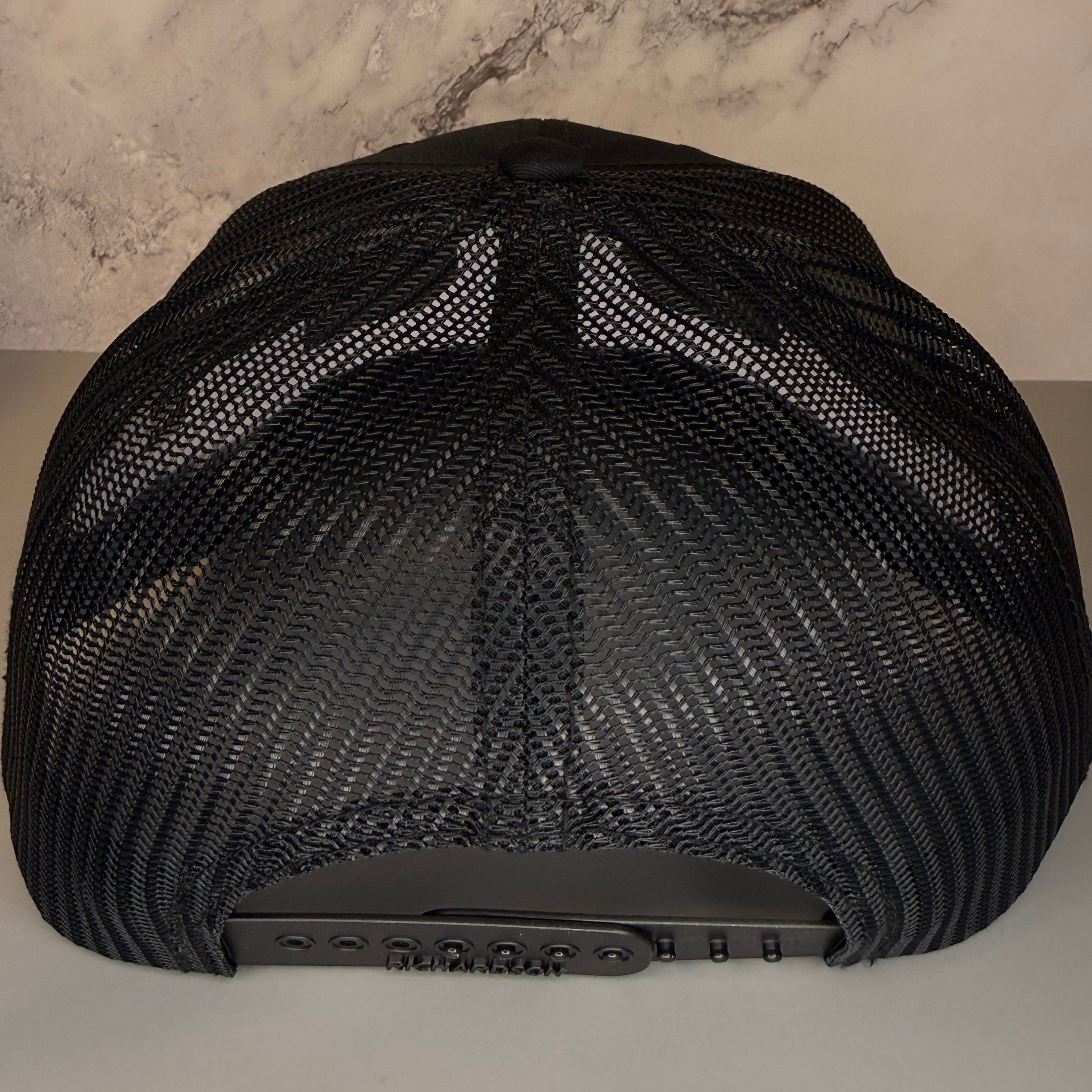 Black mesh cap on a light gray surface with a marble-patterned wall in the background