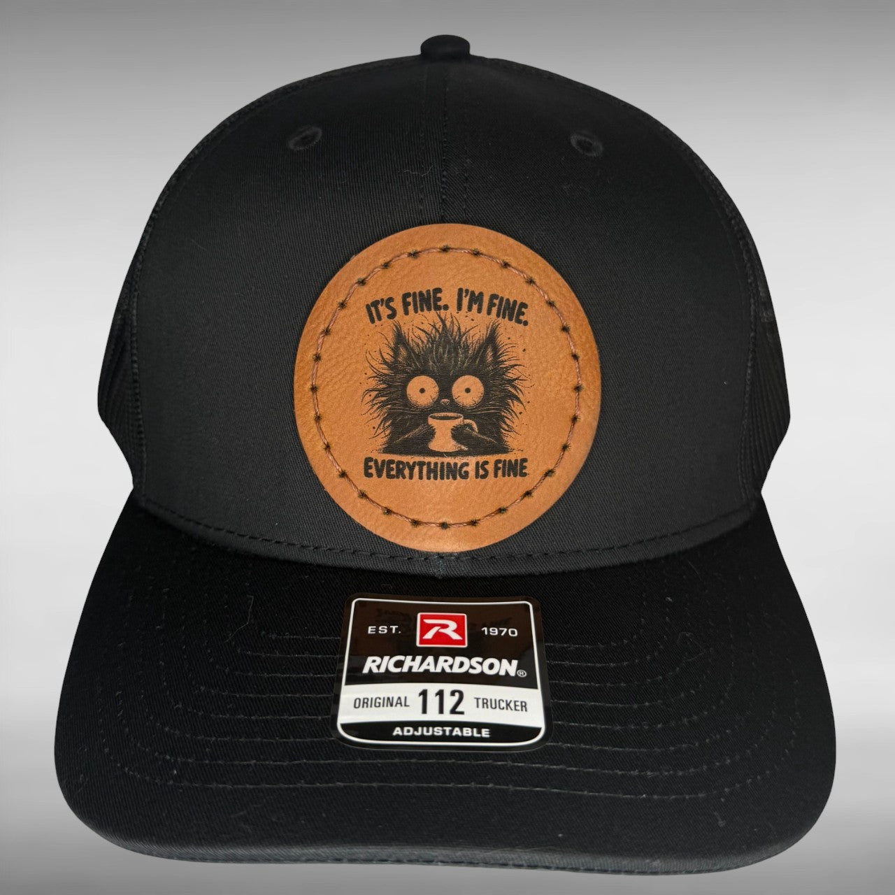 Black cap with a Richardson sticker and a brown leather patch featuring a cat and coffee design with the phrase 
