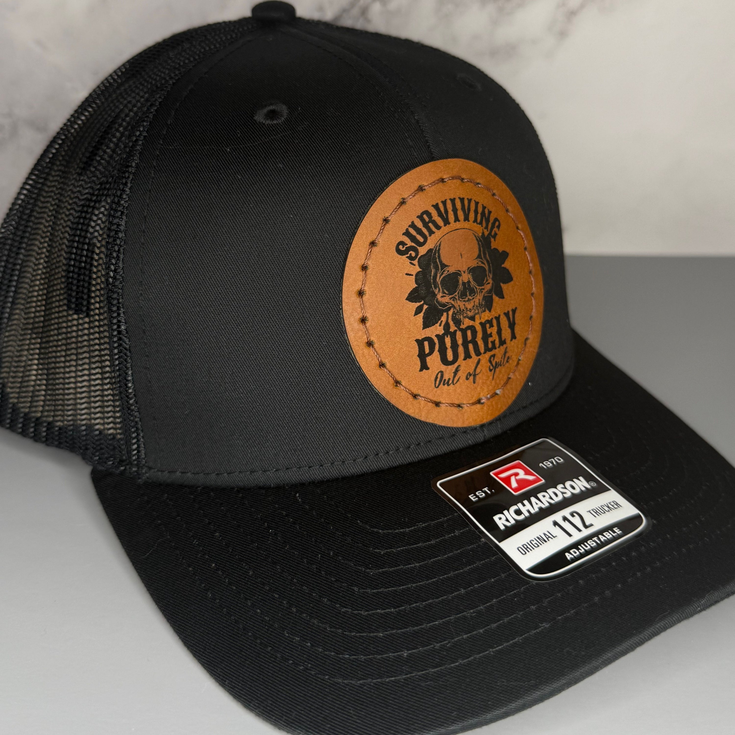 Black cap with a Richardson sticker and a brown leather patch featuring a skull and flowers design with the phrase 