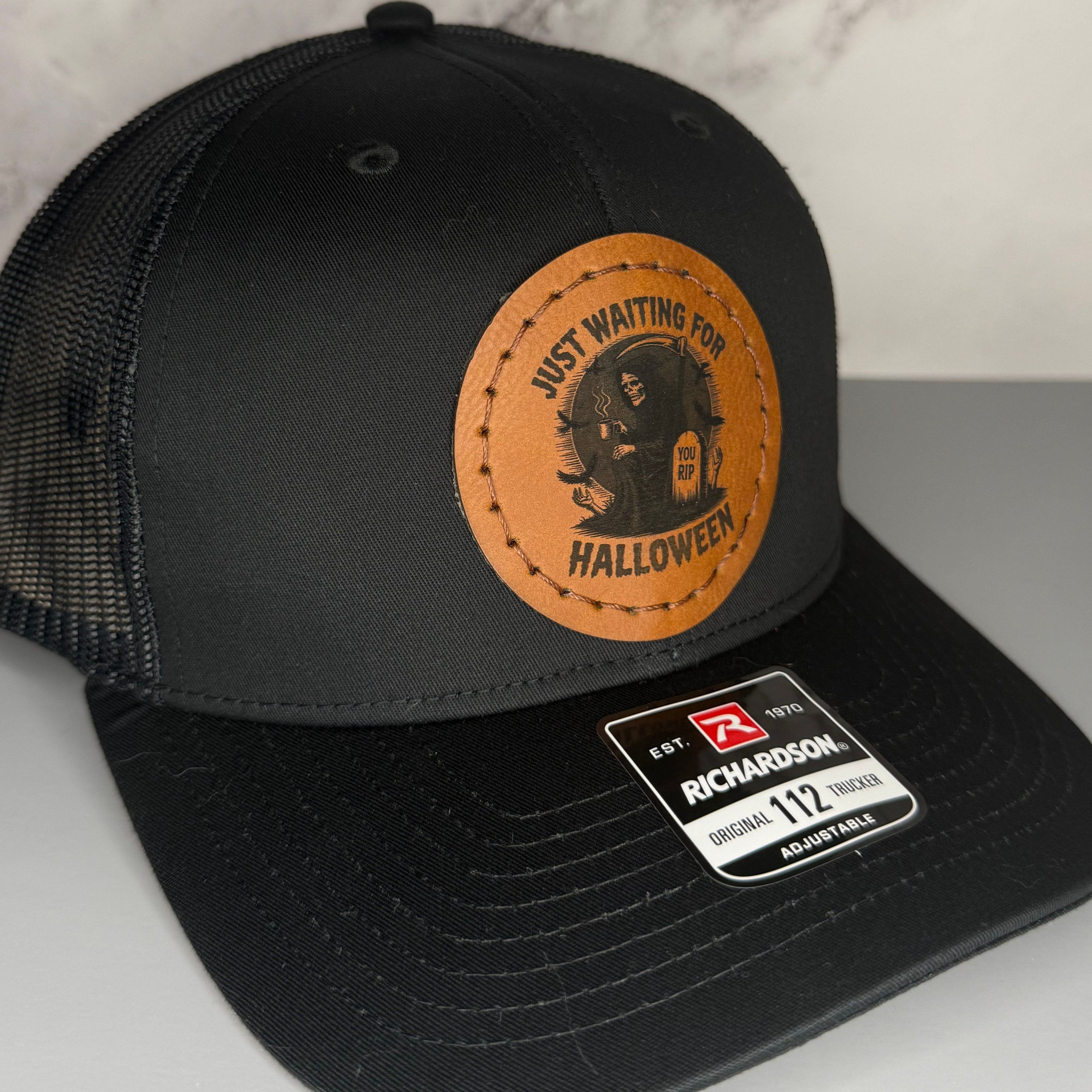 Black cap with a Richardson sticker and a brown leather patch featuring a grim reaper design with the phrase 