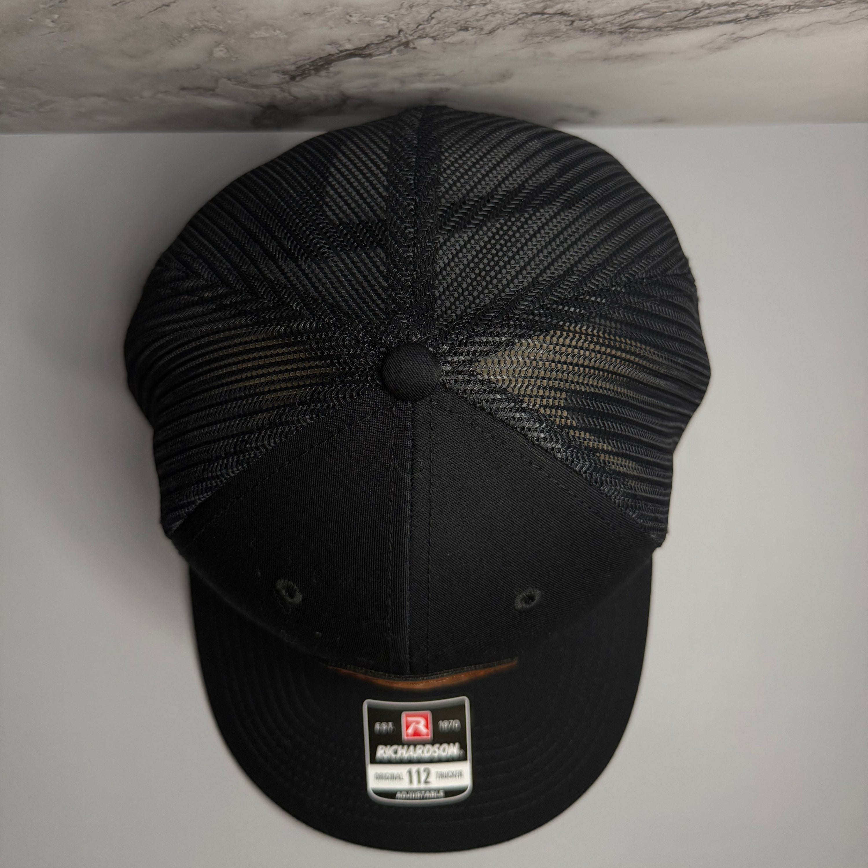 Top of a black mesh cap with Richardson sticker on a light gray background