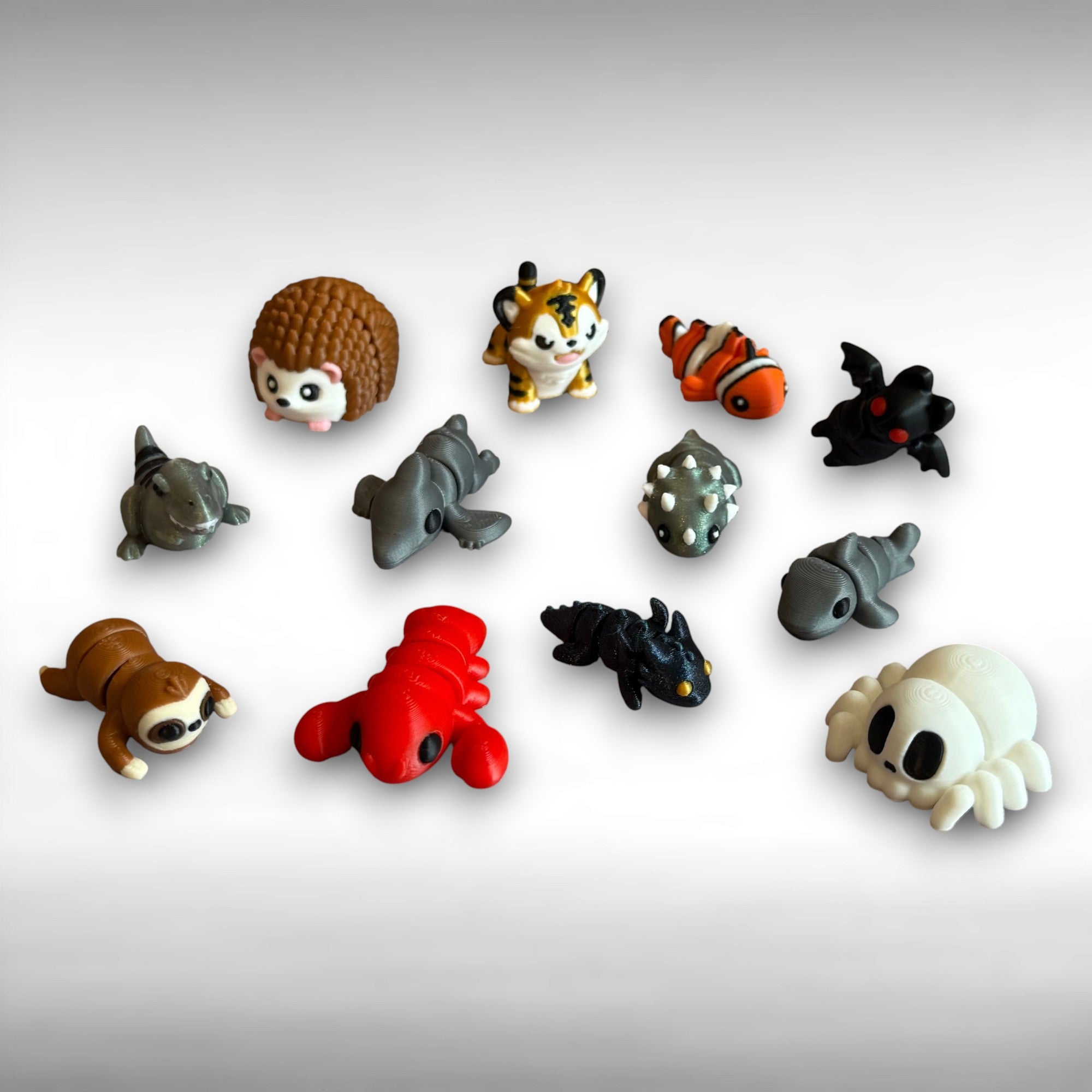 Collection of small animal figurines on a light gray background. T-rex, hedgehog, sloth, pterodactyl, tiger, lobster, dragon, triceratops, clown fish, bat, shark, and spider-shaped skeleton are featured. 