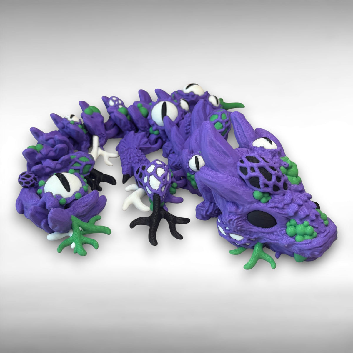 Purple and green 3D printed dragon with multiple eyes and growth-like features all over its body, against a gray background