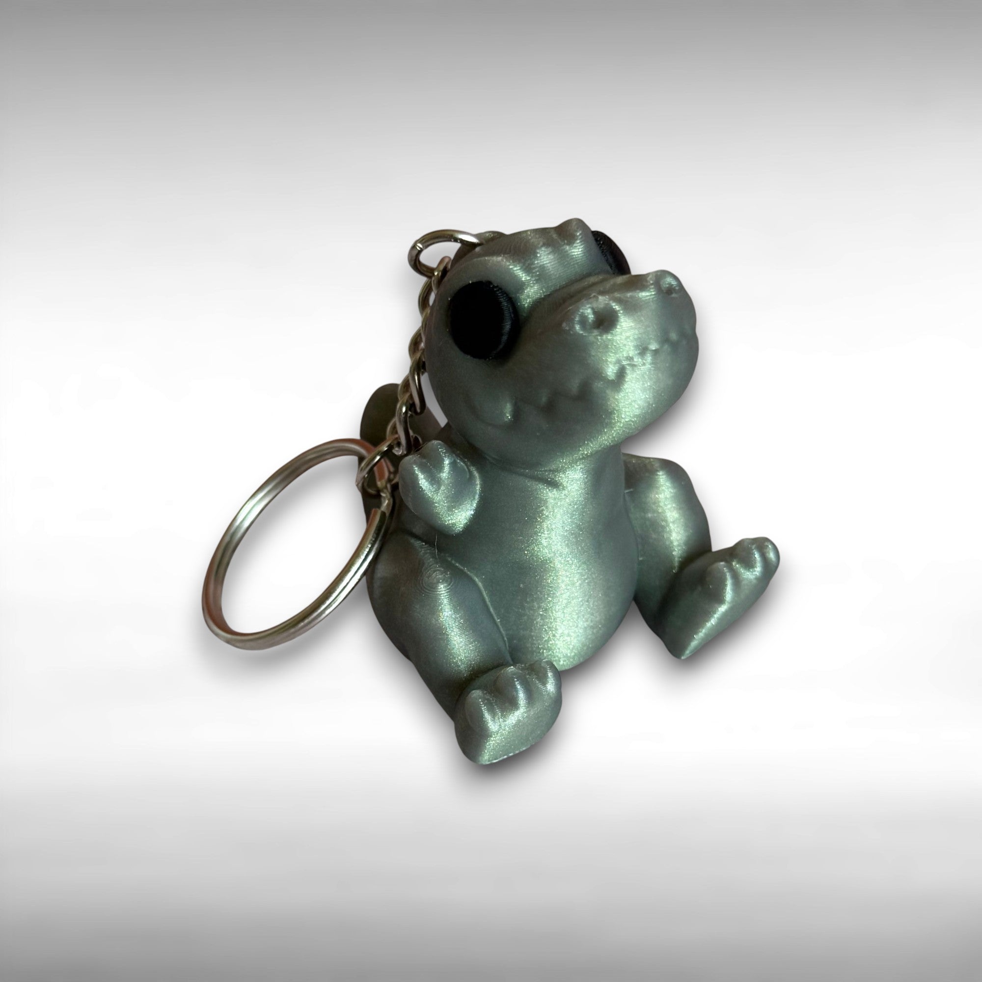 3D printed shimmer-green T-Rex dinosaur keychain on a white background