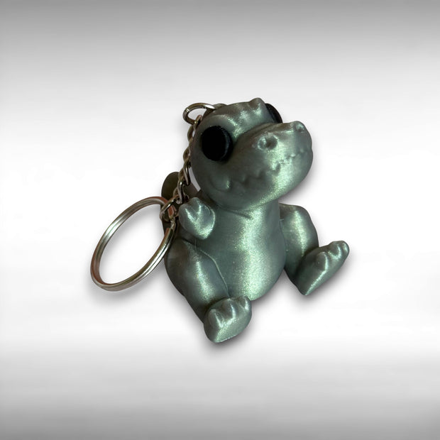 3D printed shimmer-green T-Rex dinosaur keychain on a white background
