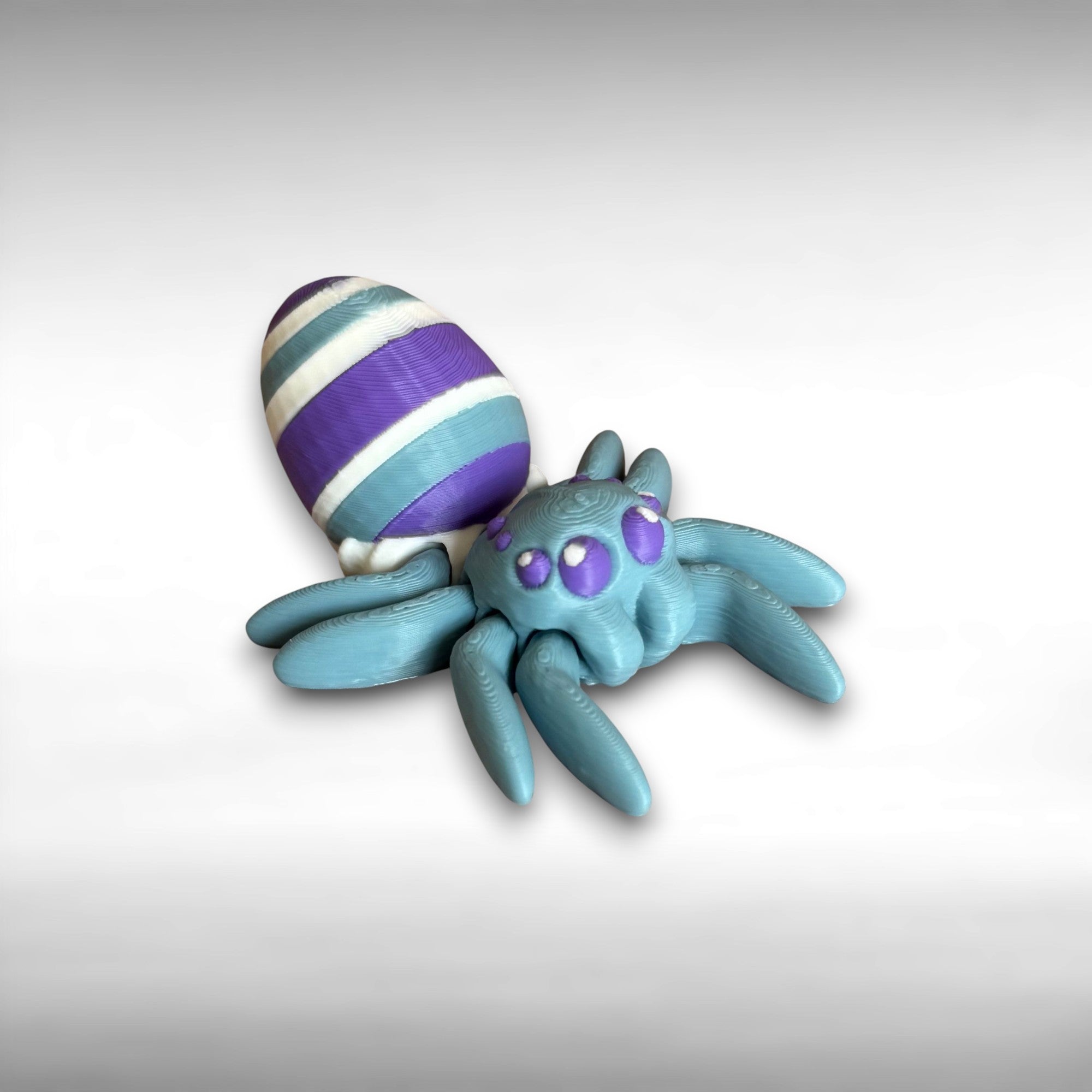 3D printed blue spider featuring a white, blue, and purple egg on its body, shown against a white background
