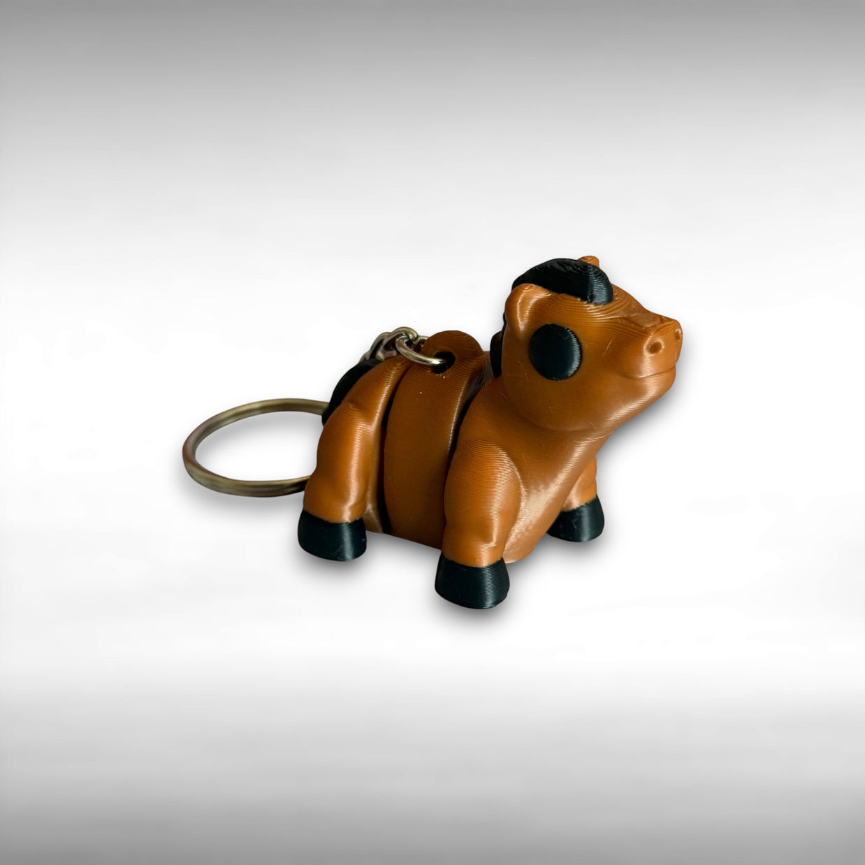 3D printed brown and black horse-shaped keychain on a gray background